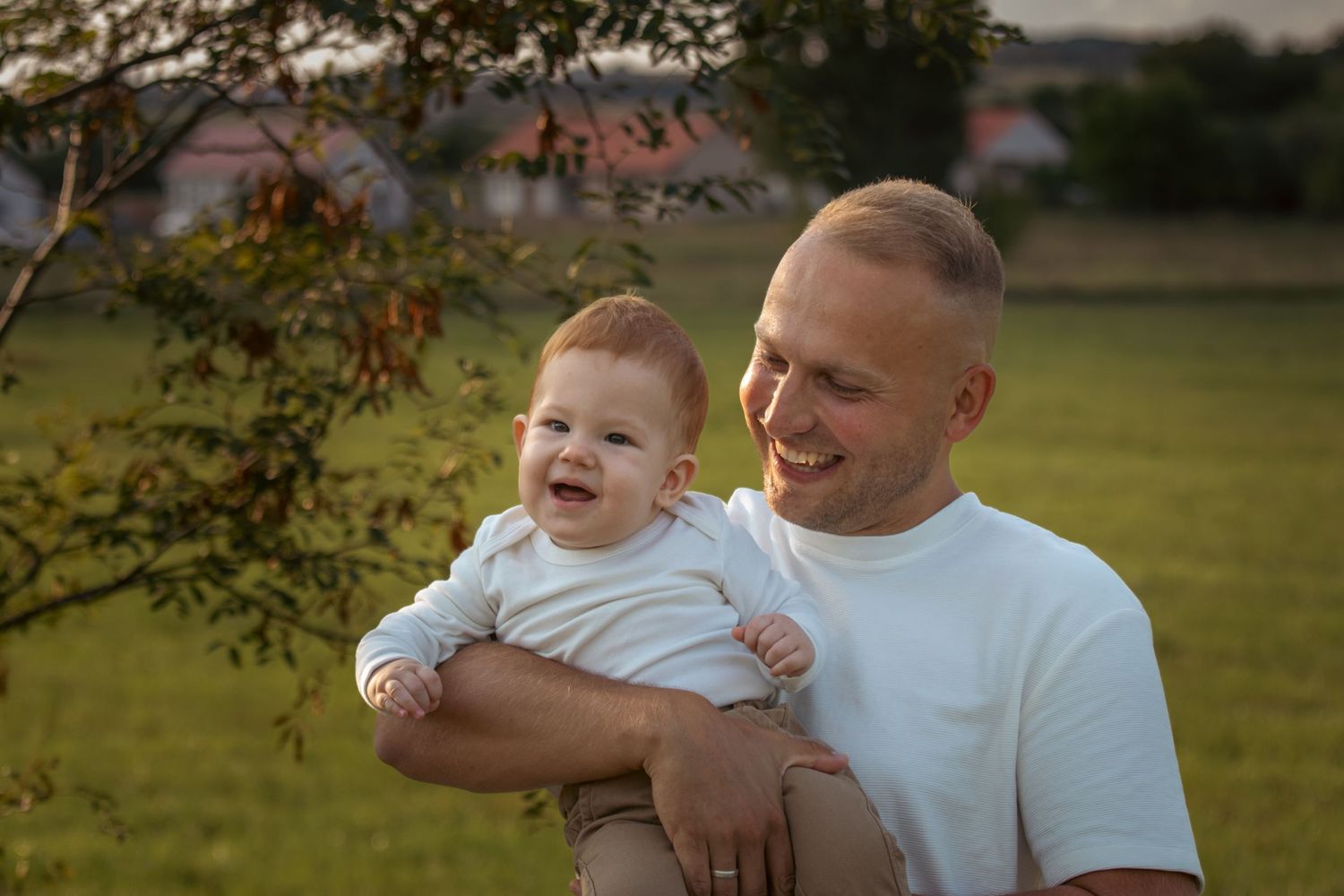 mosolygó apa nevető babával a karjában naplementében egy mezőn