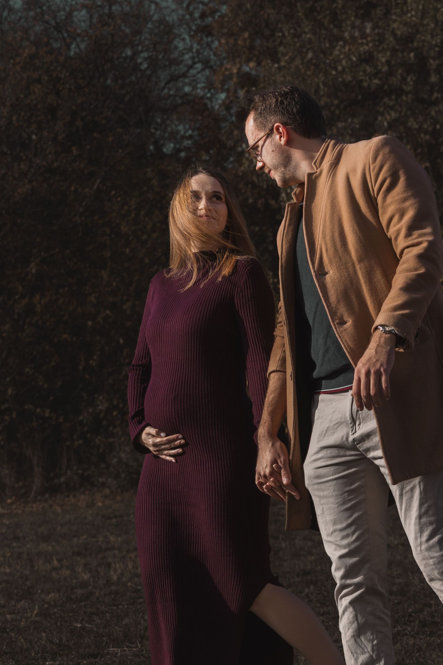 kismama bordó ruhában kézen fogva áll párjával egy őszi helyszínen