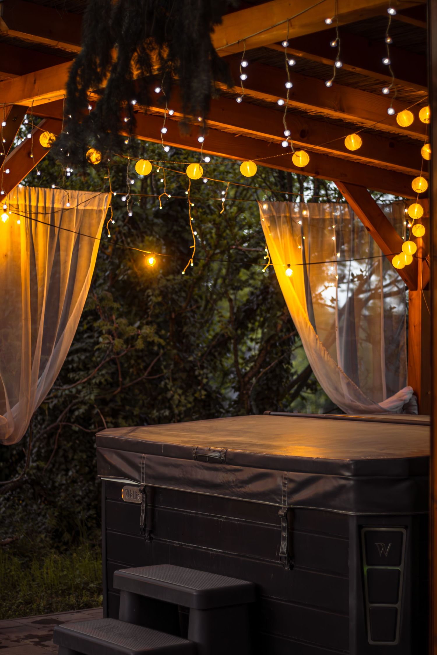 Hangulatos kültéri jacuzzi fából készült tető alatt, kis melegfényű lampionokkal és fényekkel.