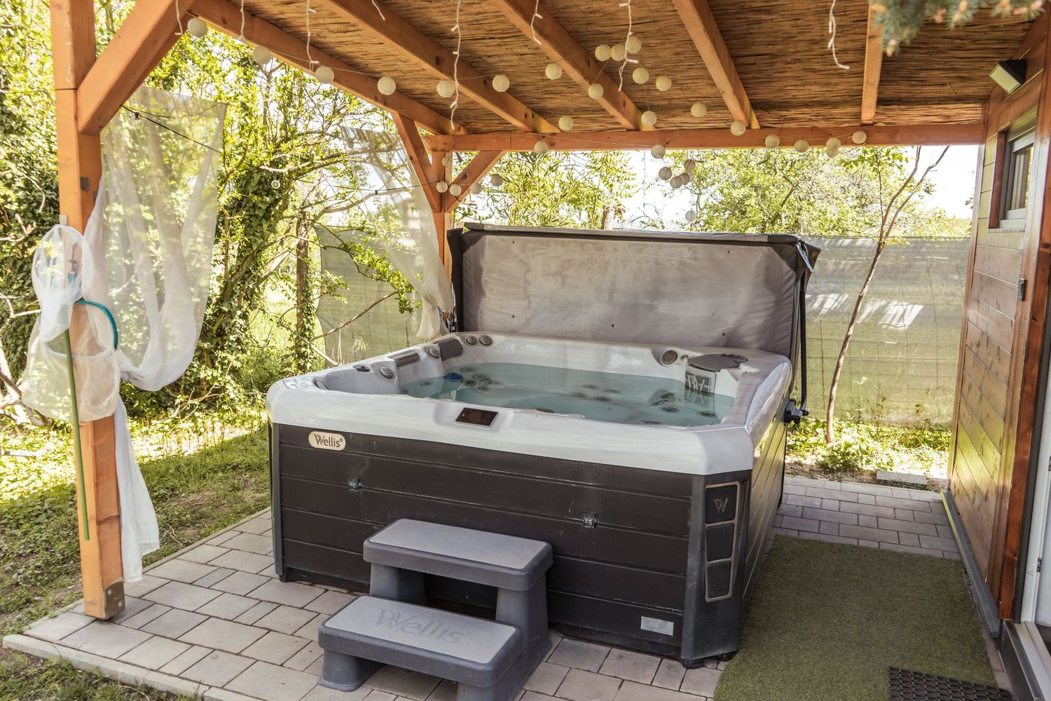 Hangulatos kültéri jacuzzi fából készült tető alatt, kis melegfényű lampionokkal és fényekkel.