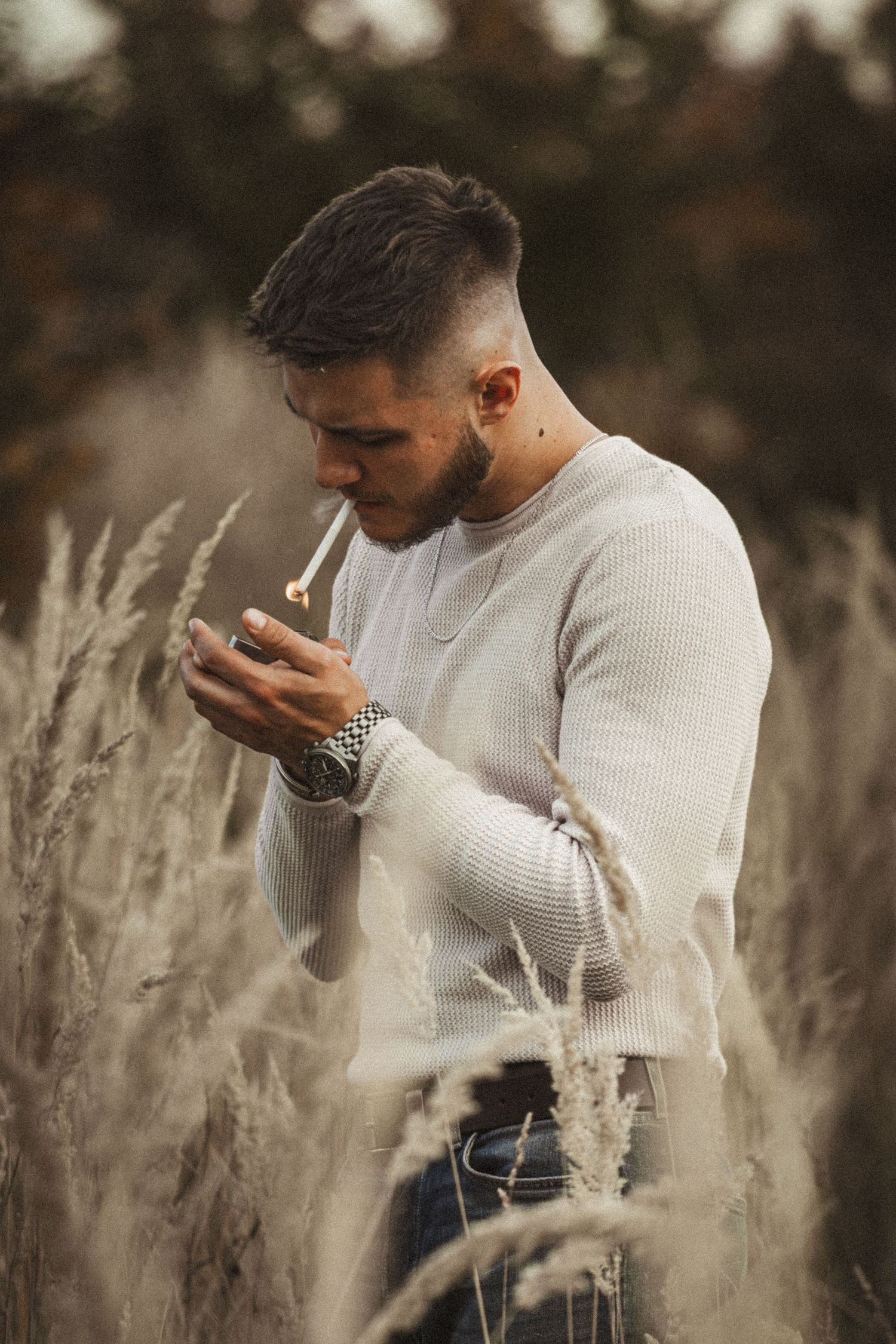 férfi fehér pulcsiban cigarettát gyújt a szabadban