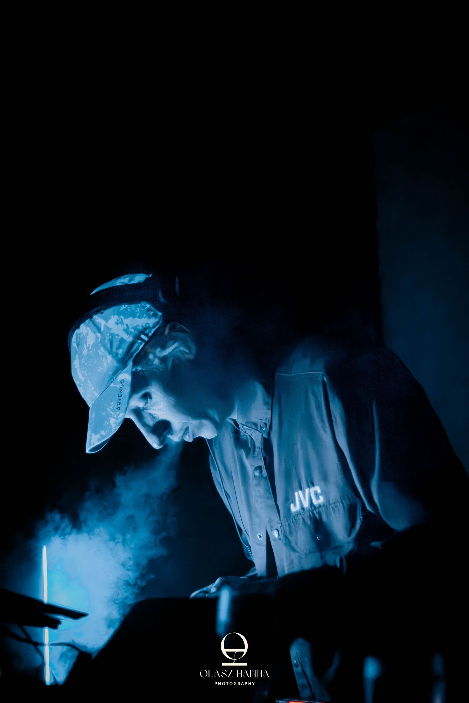 DJ kék fényekben és füstben zenél egy színpadon sapkában és pólóban