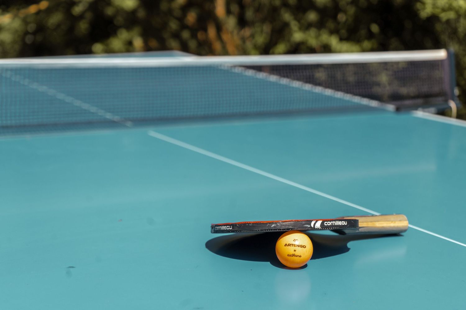 Ping pong ütő labdával pihen egy kék ping pong asztalon..