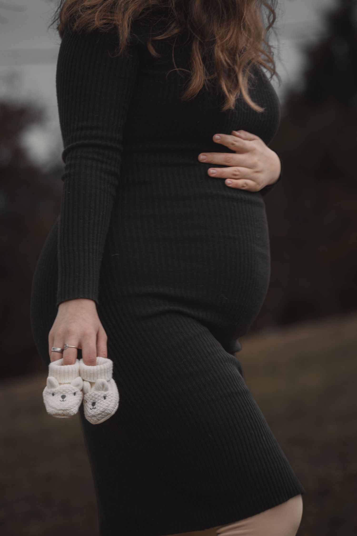 kismama fekete ruhában apró kötött babacipőt tart a kezében