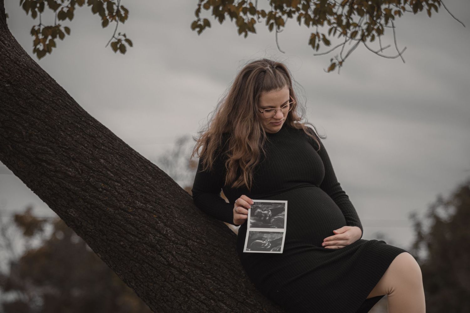 kismama fekete ruhában faágon ülve ultrahang képet tart a kezében