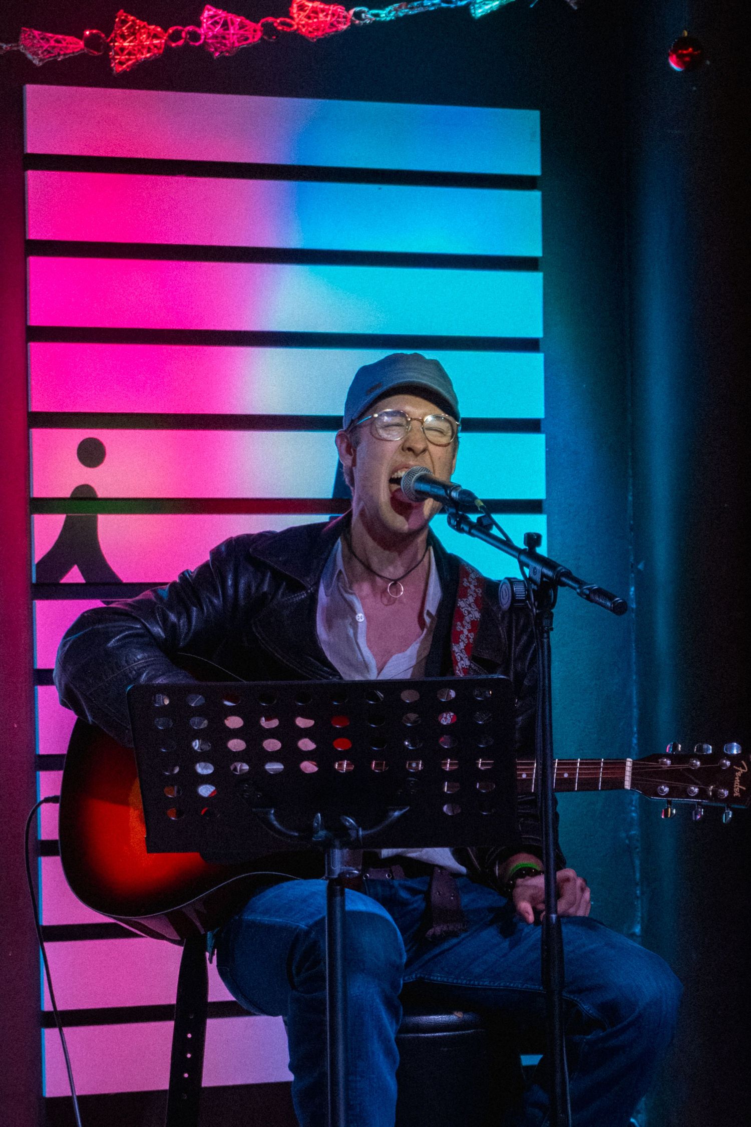 zenész akusztikus gitáron játszik és énekel neonfényes színpadon