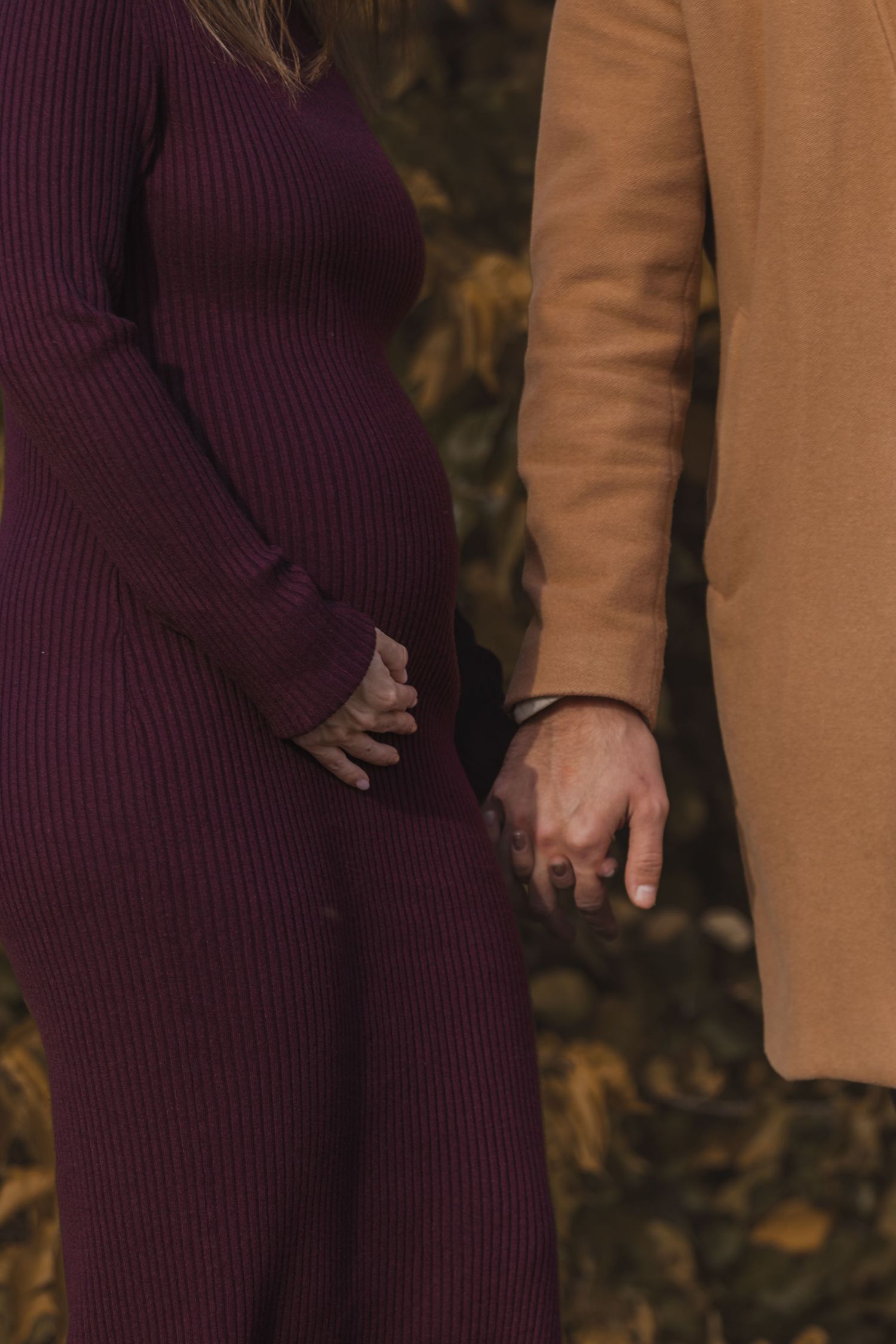 kismama bordó ruhában párjával kézen fogva egy őszi fotózáson