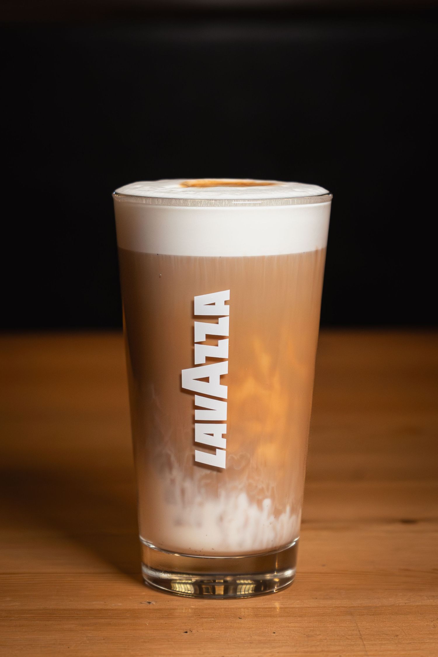 rétegezett latte macchiato Lavazza pohárban fa felületen, sötét háttérrel