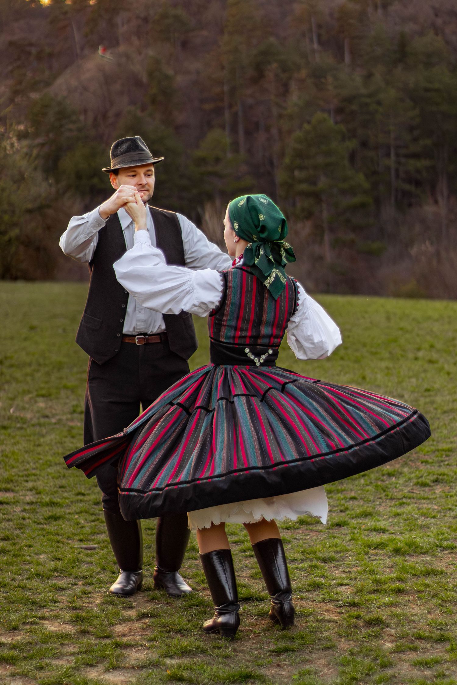 pár népviseletben táncol a szabadban, színes szoknyában és kalapban
