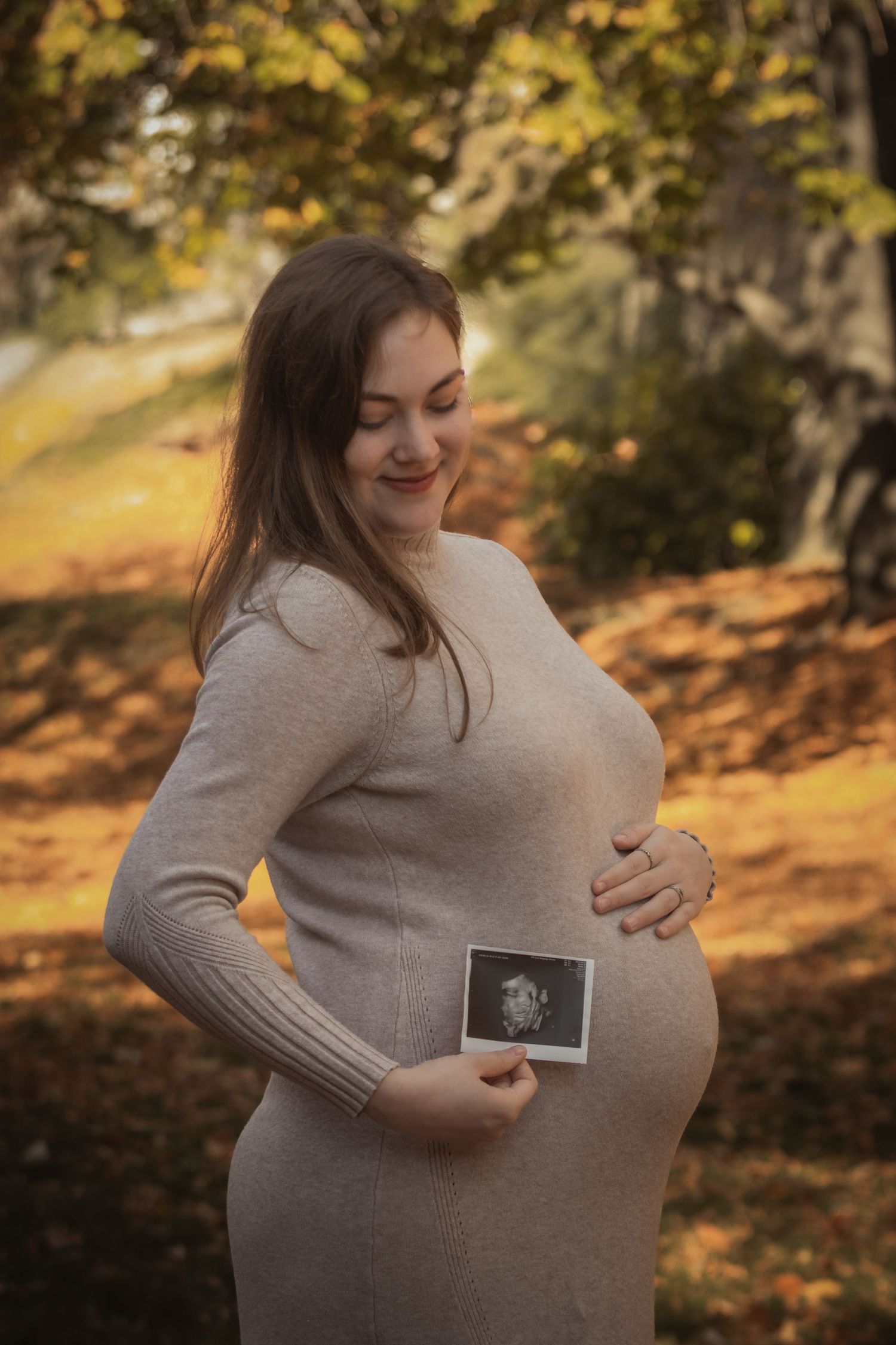kismama bézs ruhában ultrahang képet néz mosolyogva a pocakjára