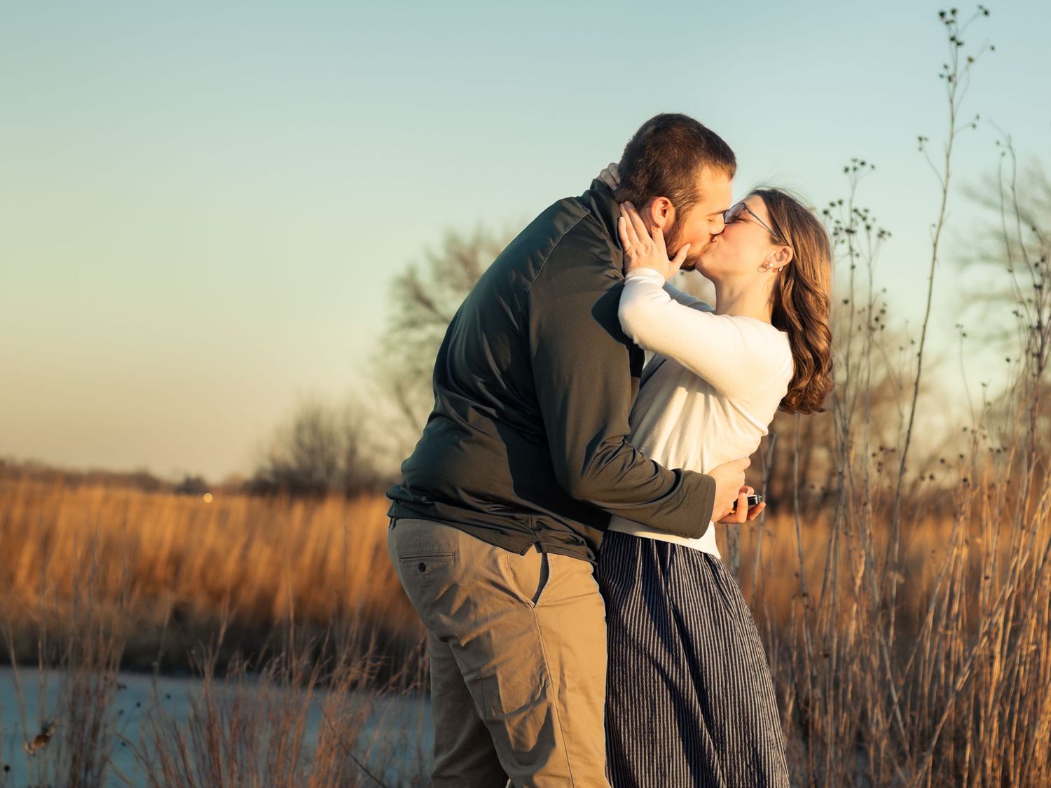 Couple sharing a romantic kiss outdoors in golden hour light near tall grass.