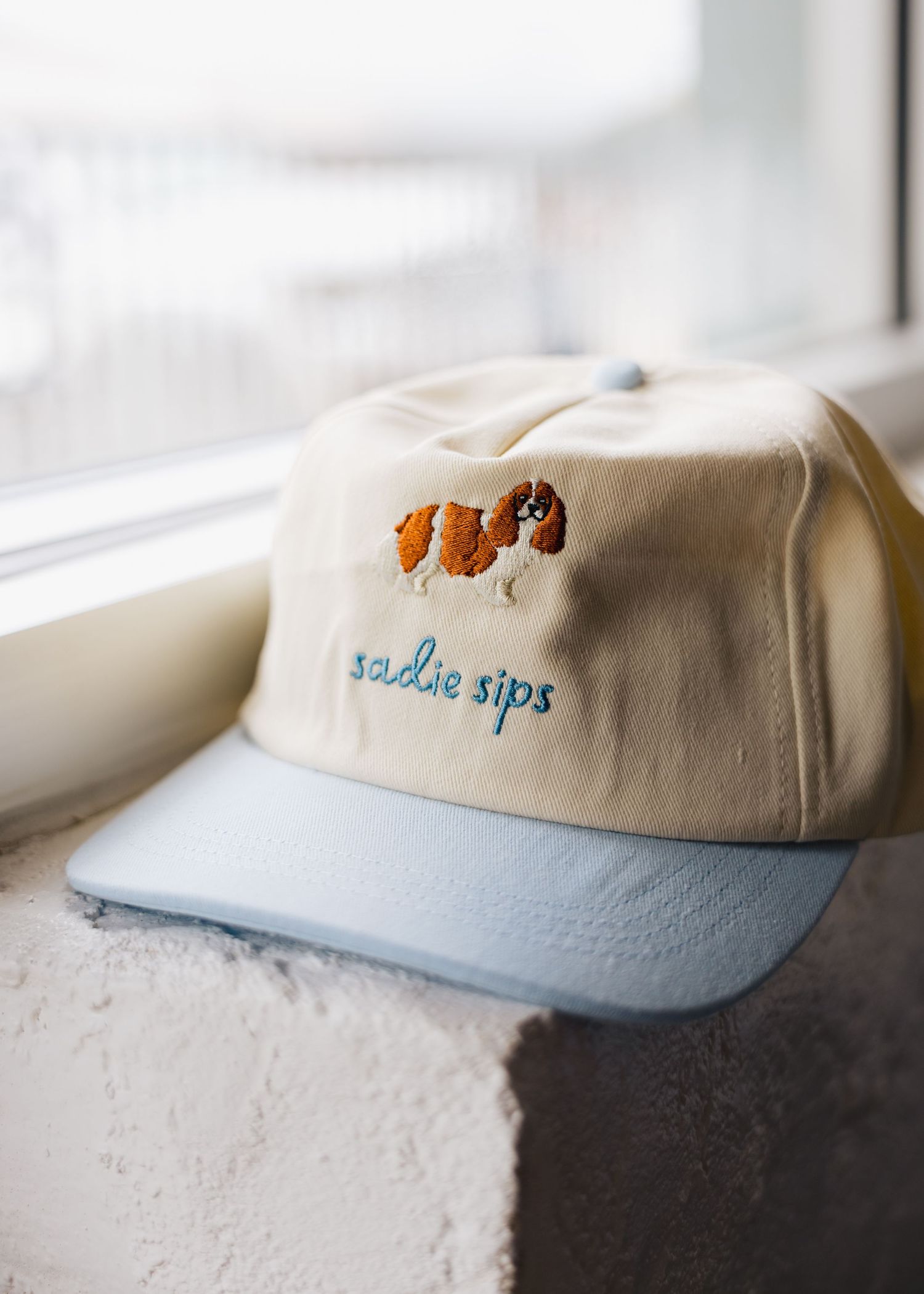 Cream and light blue snapback hat with embroidered Cavalier King Charles Spaniel and Sadie Sips text.