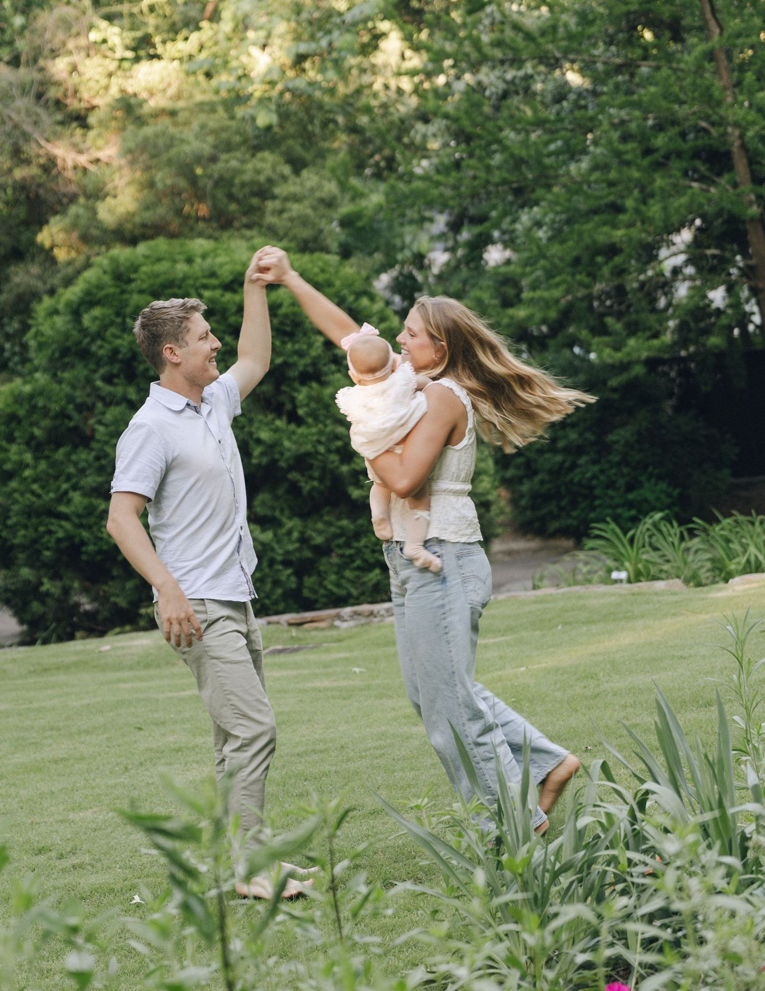 Happy couple dancing outdoors in green garden while holding their baby.