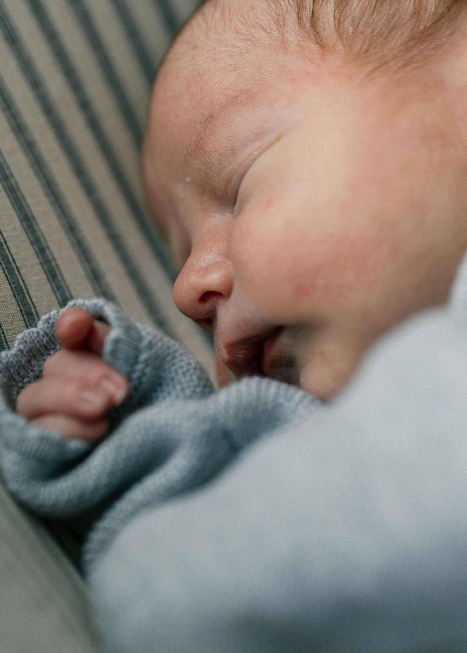 Close-up of peaceful sleeping newborn baby in light blue outfit on striped surface.