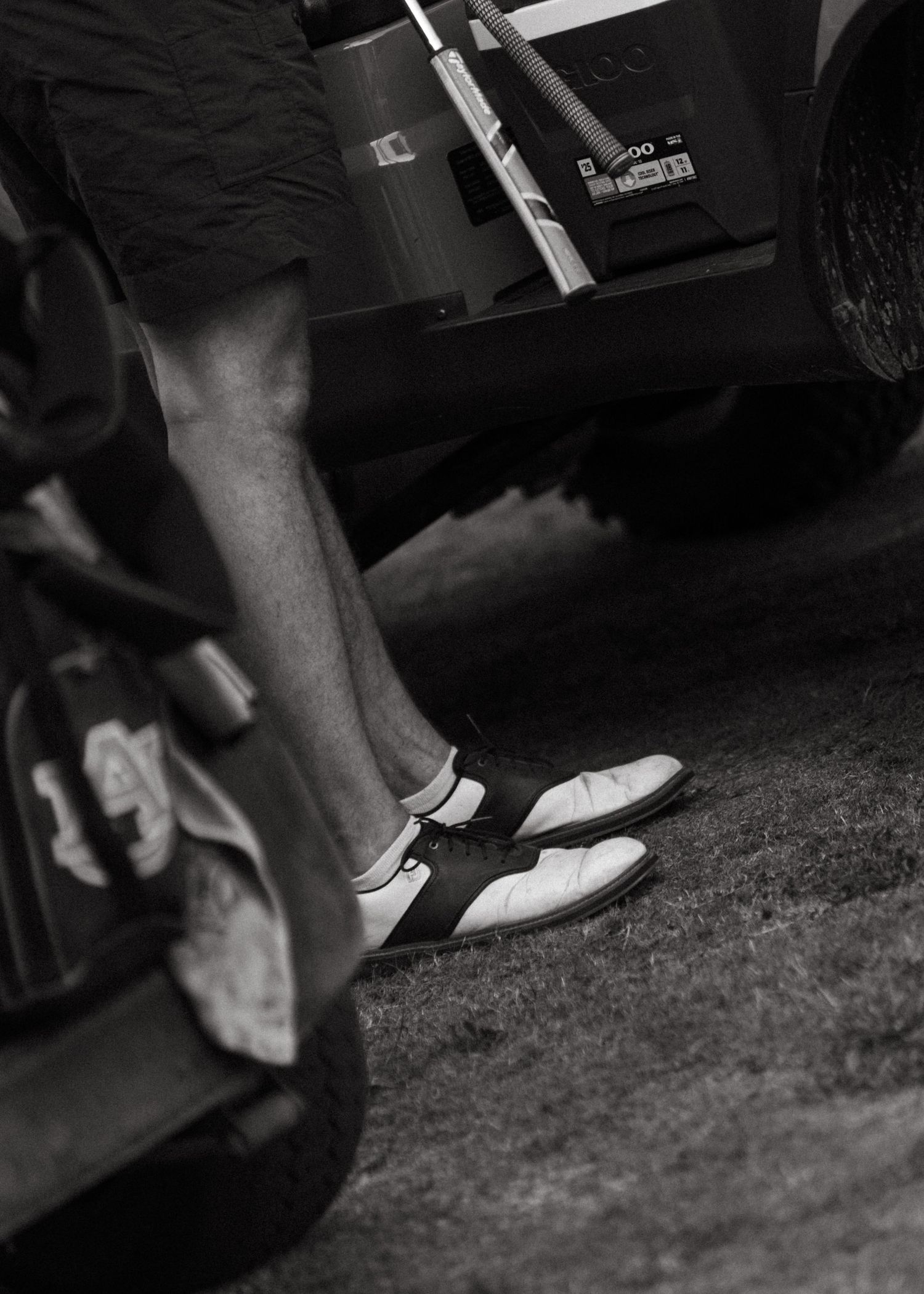 Black and white close-up of golfer wearing classic saddle shoes near golf cart.