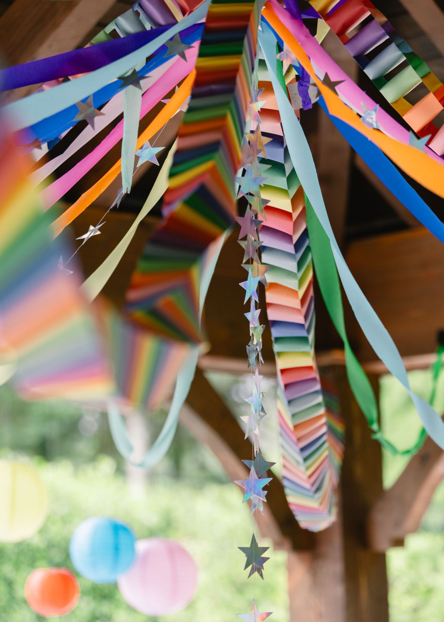Colorful rainbow paper streamers and star garlands hang from a decorated outdoor party pavilion.