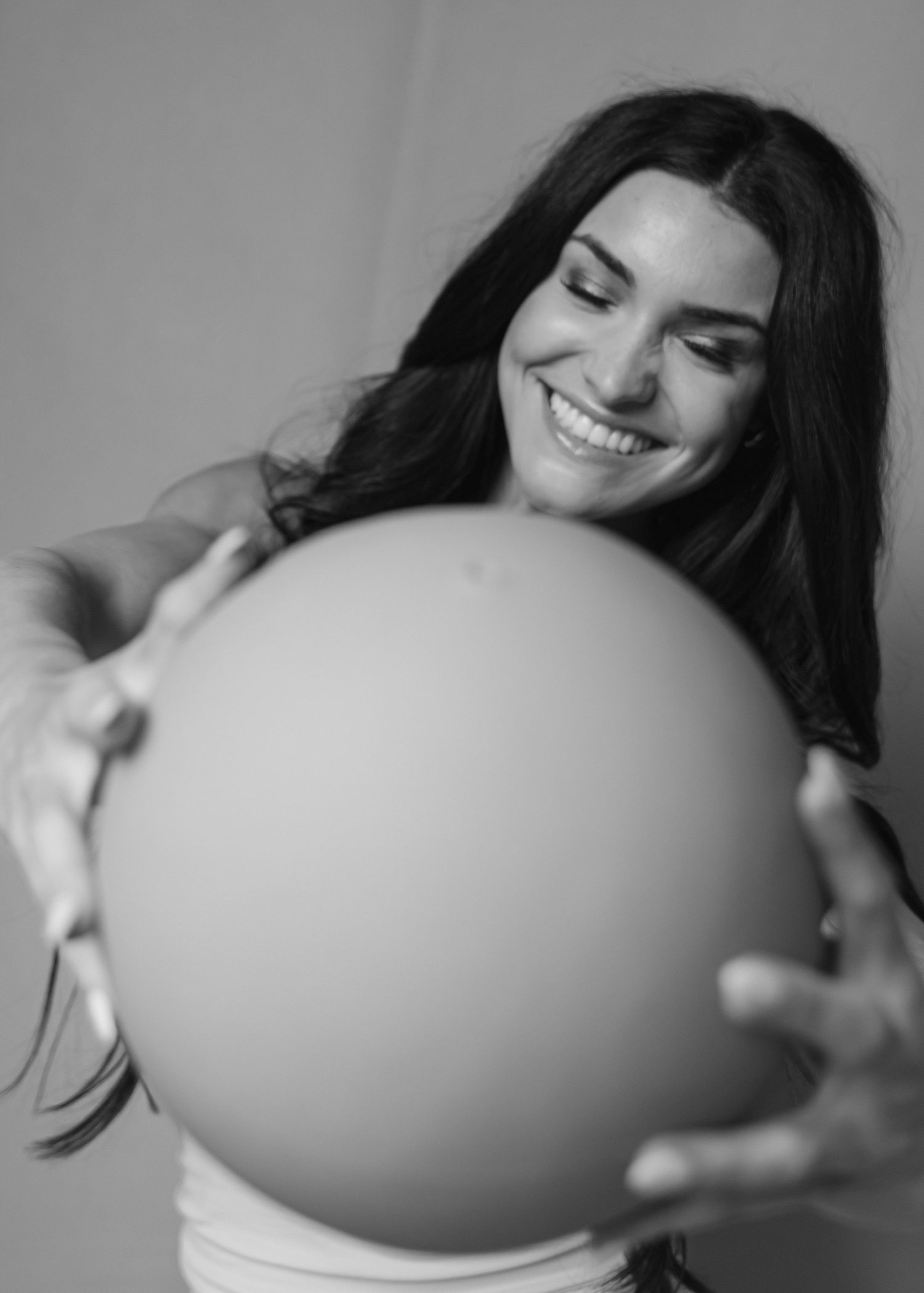Black and white photo of smiling brunette woman holding large exercise ball forward.