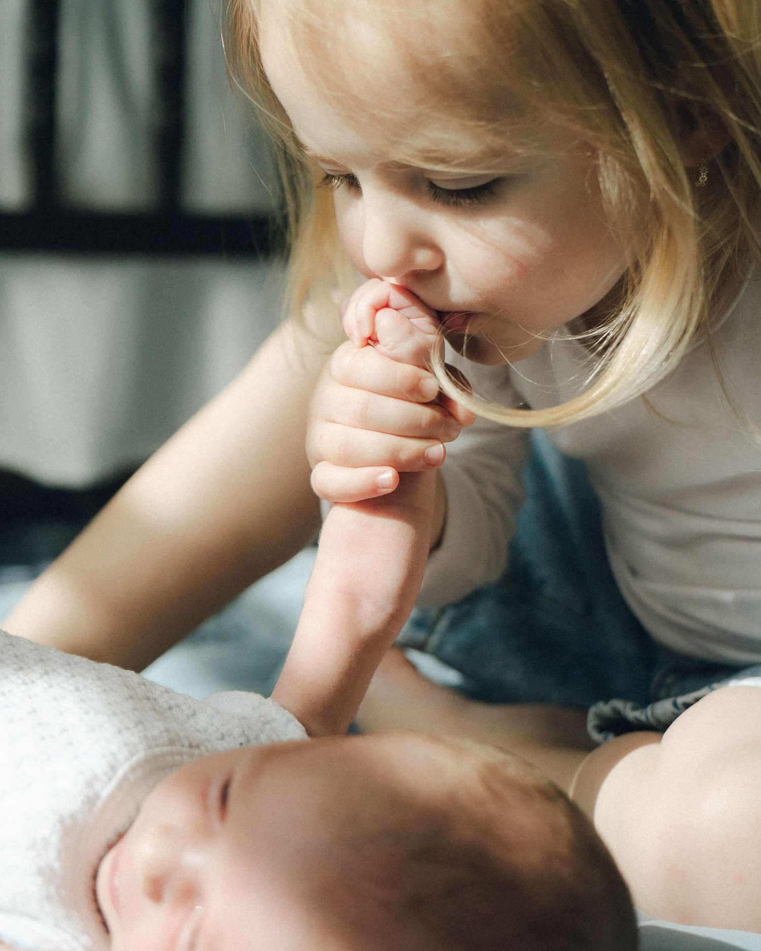 Young child kissing newborn baby sibling's hand in tender moment.