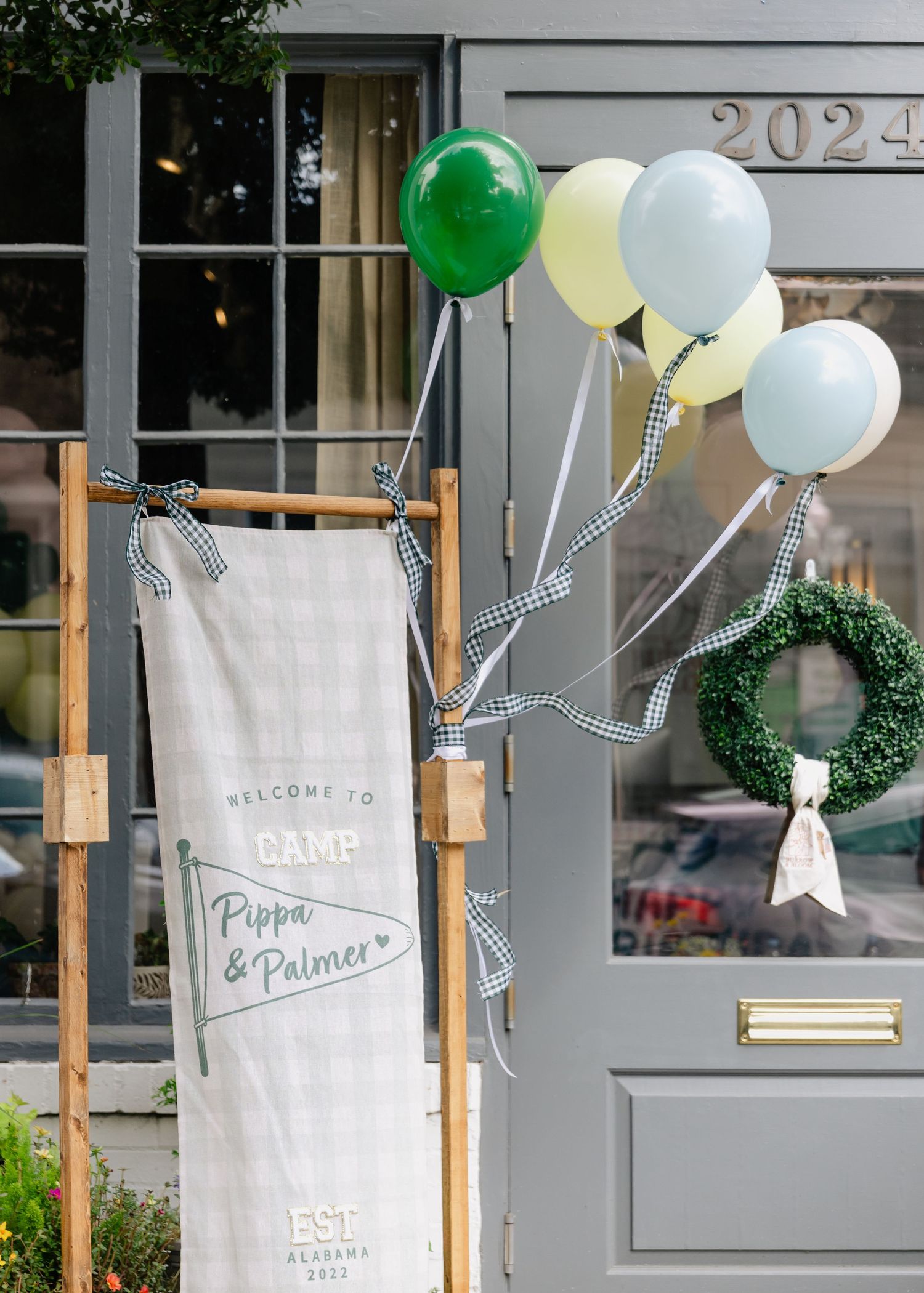 Camp Pippa and Palmer welcome sign with green and yellow balloons decorating a gray door entrance.