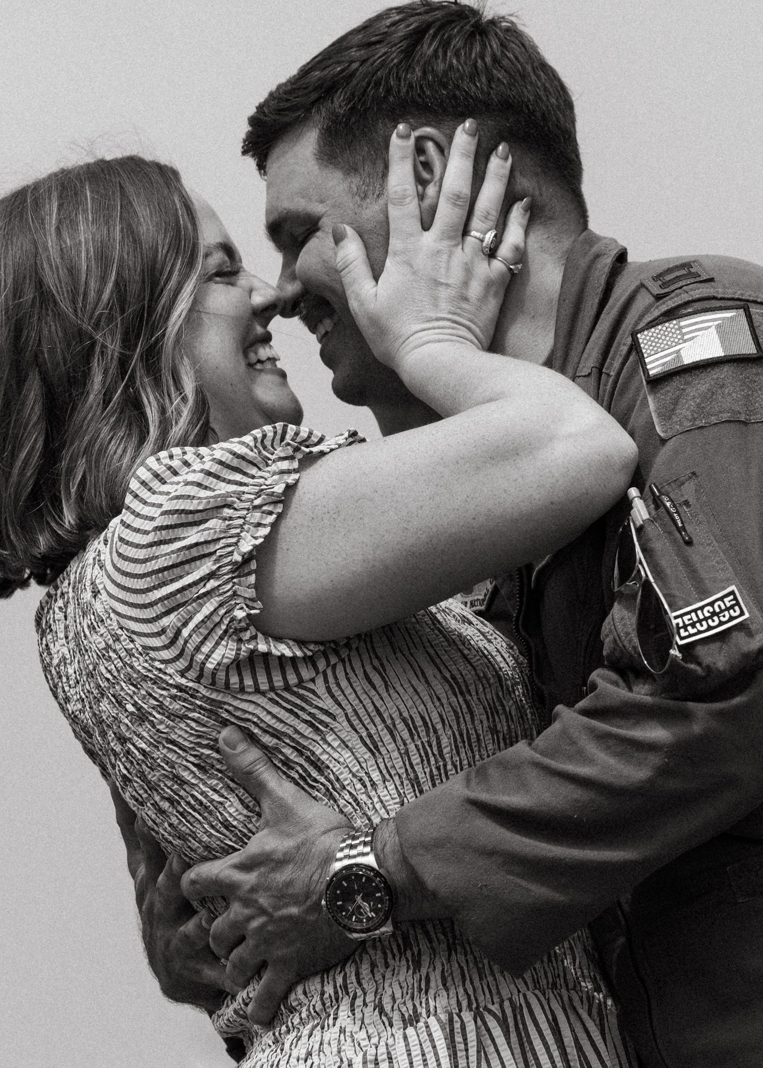 Black and white photo of a couple sharing an intimate moment, woman cupping man's face in military flight suit.