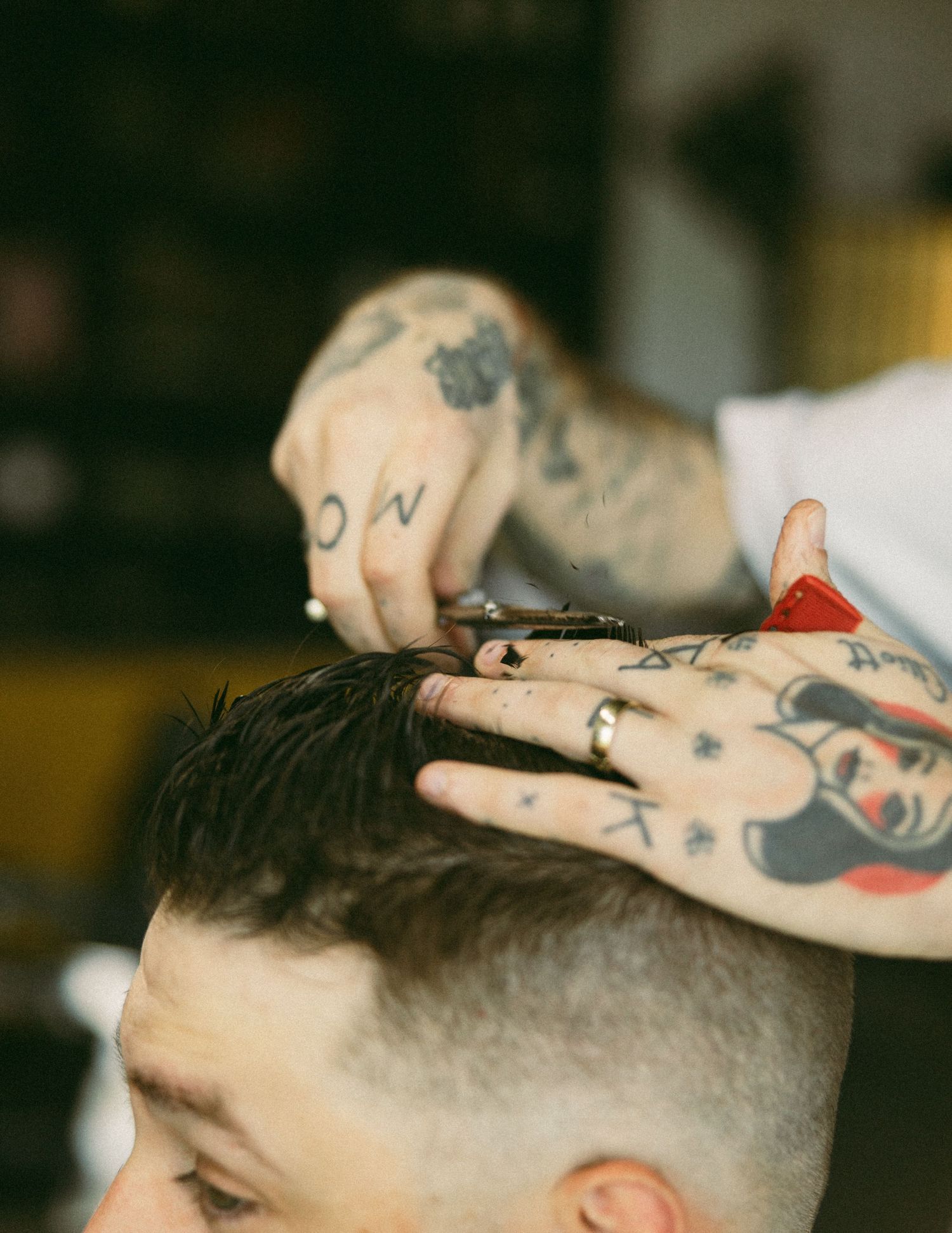 Tattooed barber cutting a client's hair with scissors in a barbershop.