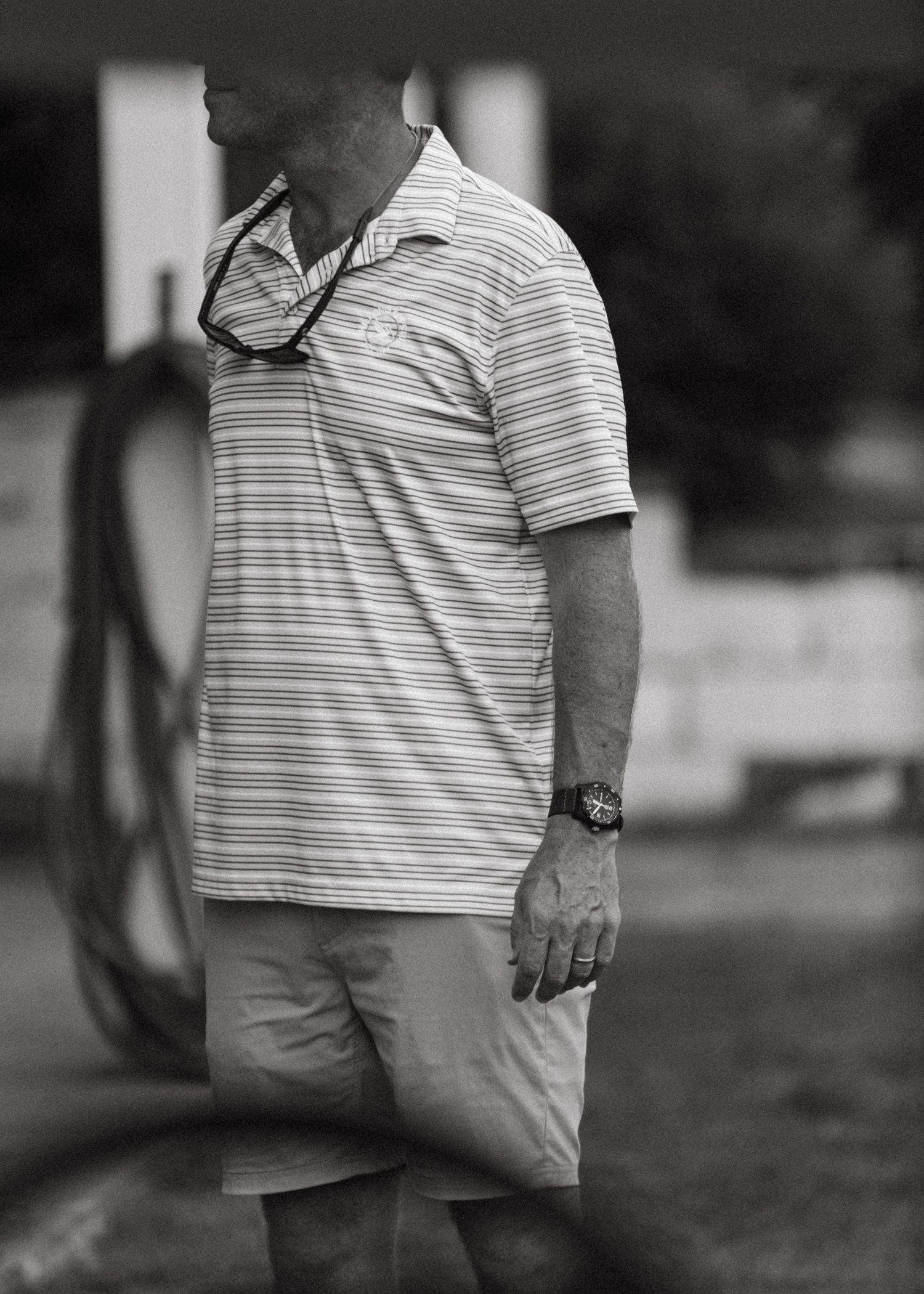 Black and white side profile of a man in a striped polo shirt and shorts on a golf course.