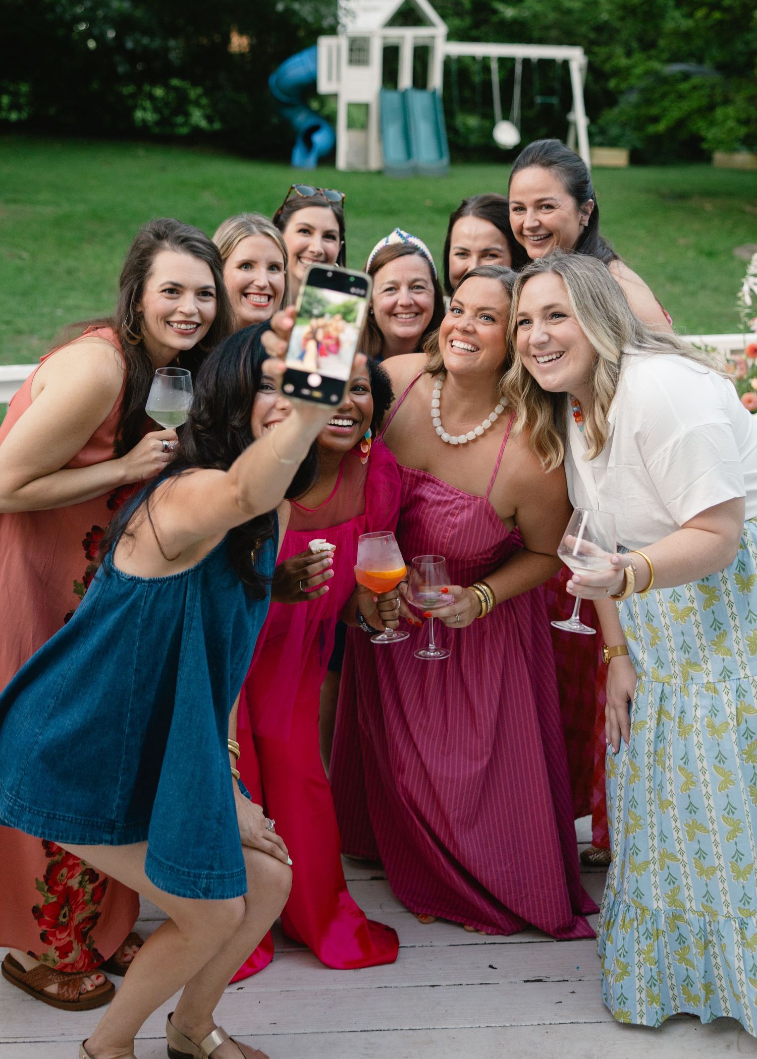 Group of smiling women taking a selfie with wine and cocktails at a summer outdoor celebration party.