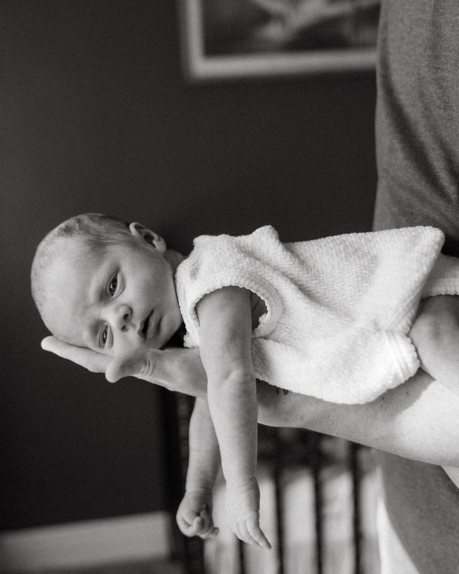 Black and white close-up of newborn baby being held by parent indoors.
