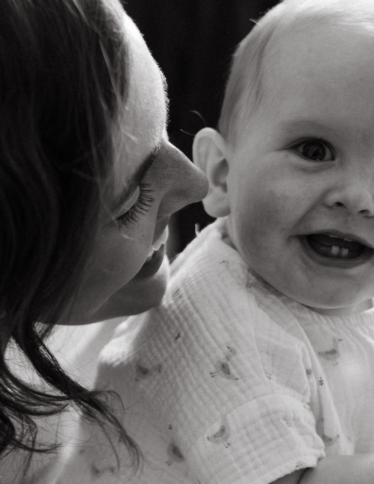 Black and white photo of a mother smiling at her laughing baby with tiny teeth.
