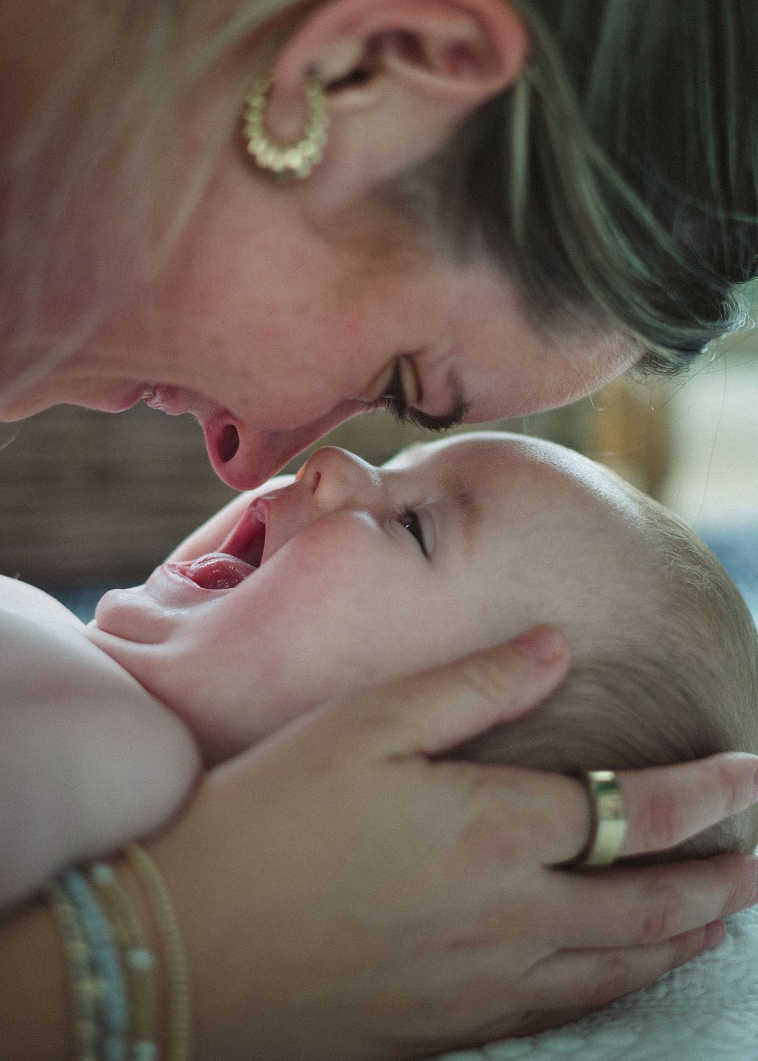 Mother tenderly touching noses with her smiling baby in a warm close-up photo.