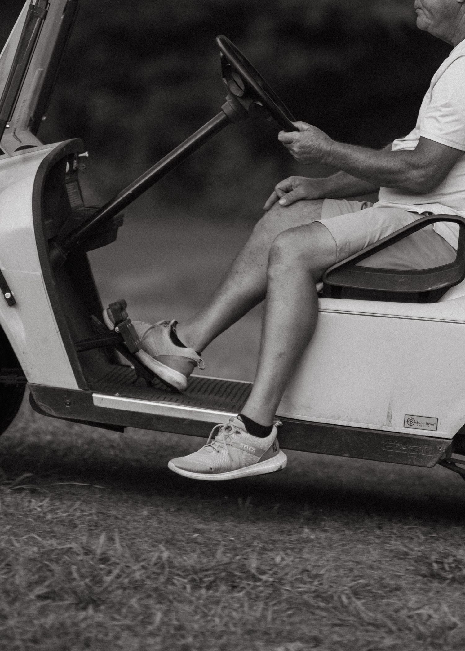 Man in shorts and sneakers sitting in a white golf cart on a golf course.