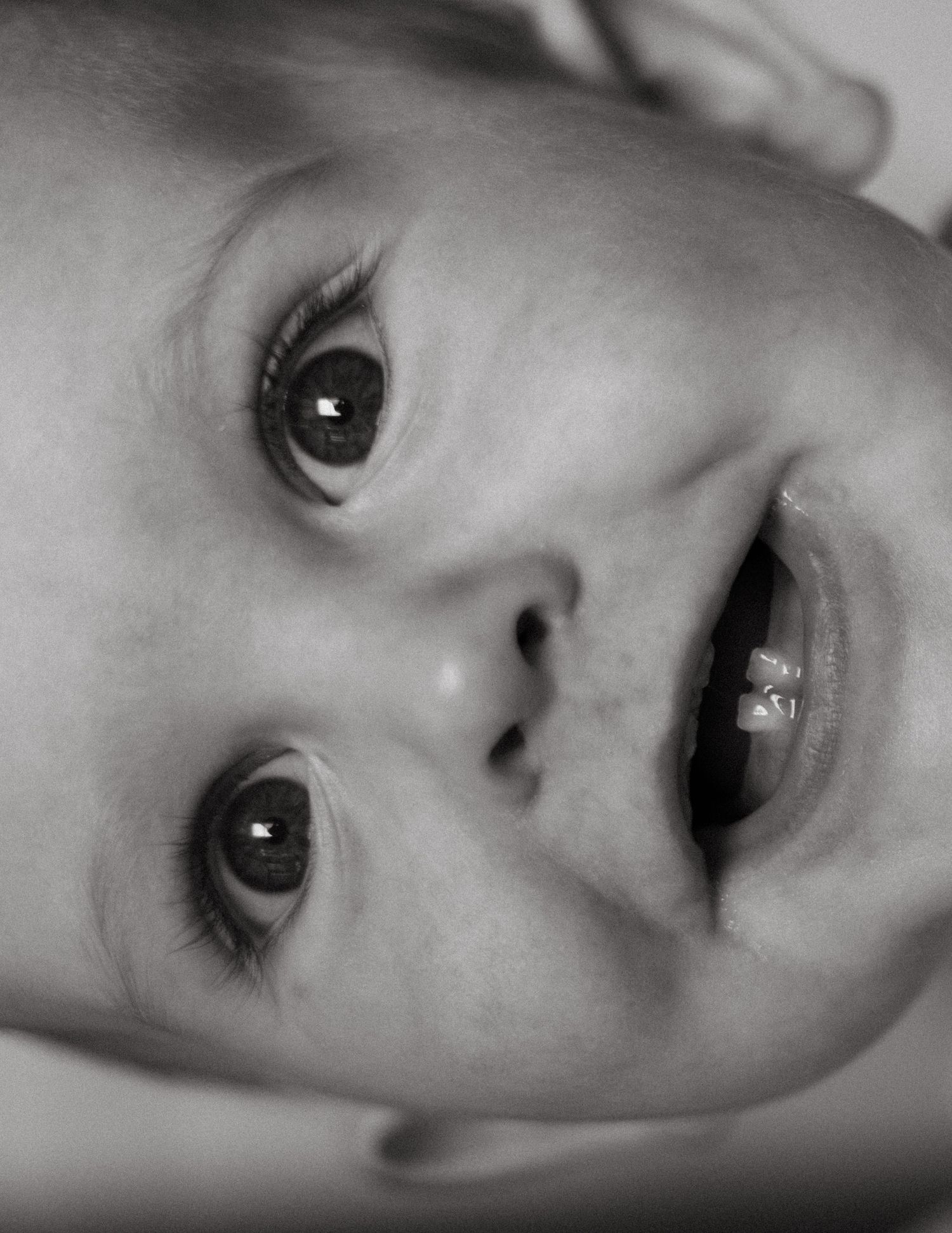 Adorable close-up black and white portrait of a baby with wide eyes and open mouth.