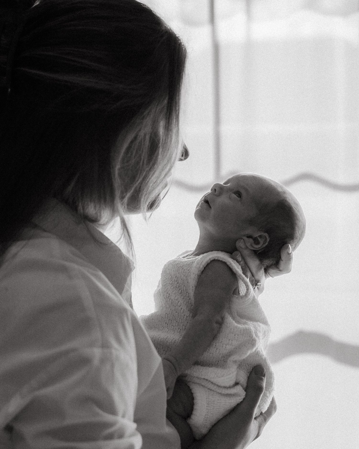 Black and white photo of mother holding alert newborn baby by window.