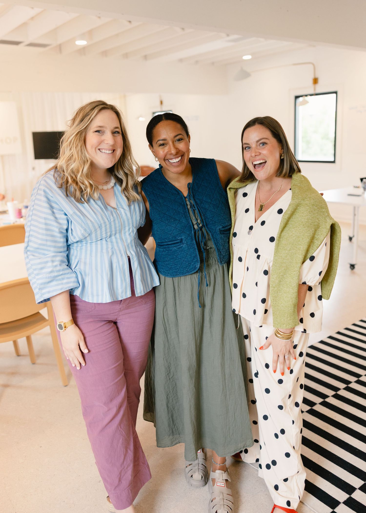 Three smiling women posing together in a modern bright studio space at a workshop.