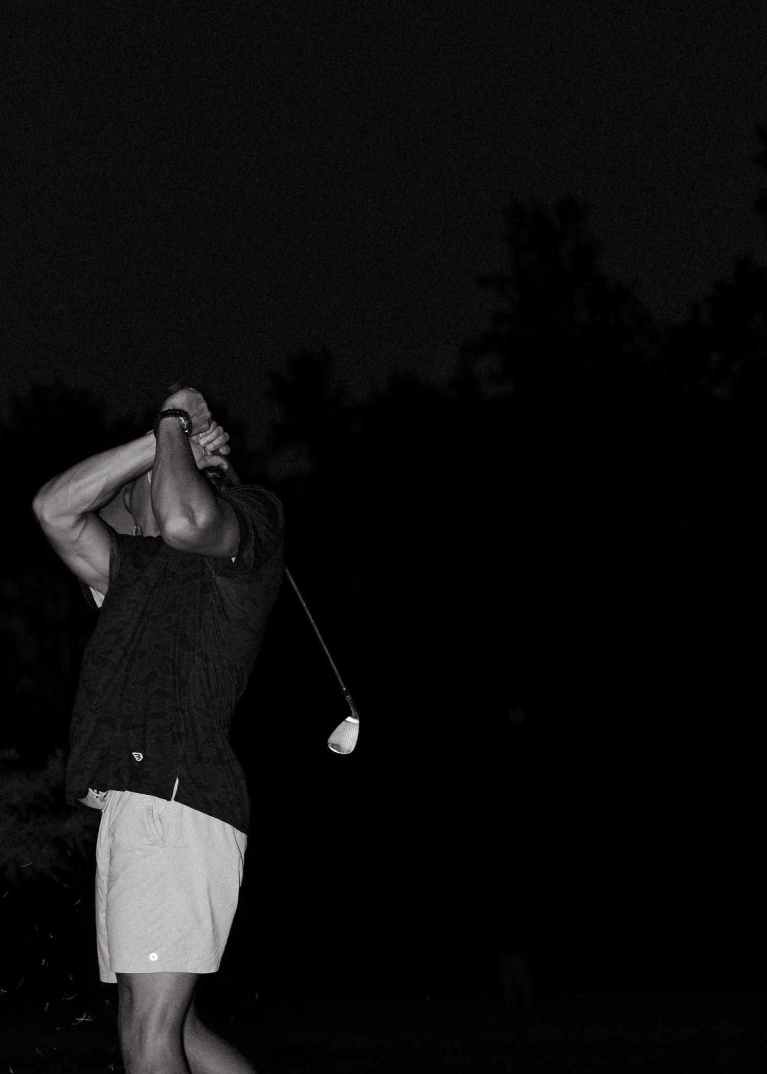 Black and white photo of a golfer completing a swing at night on a dark golf course.