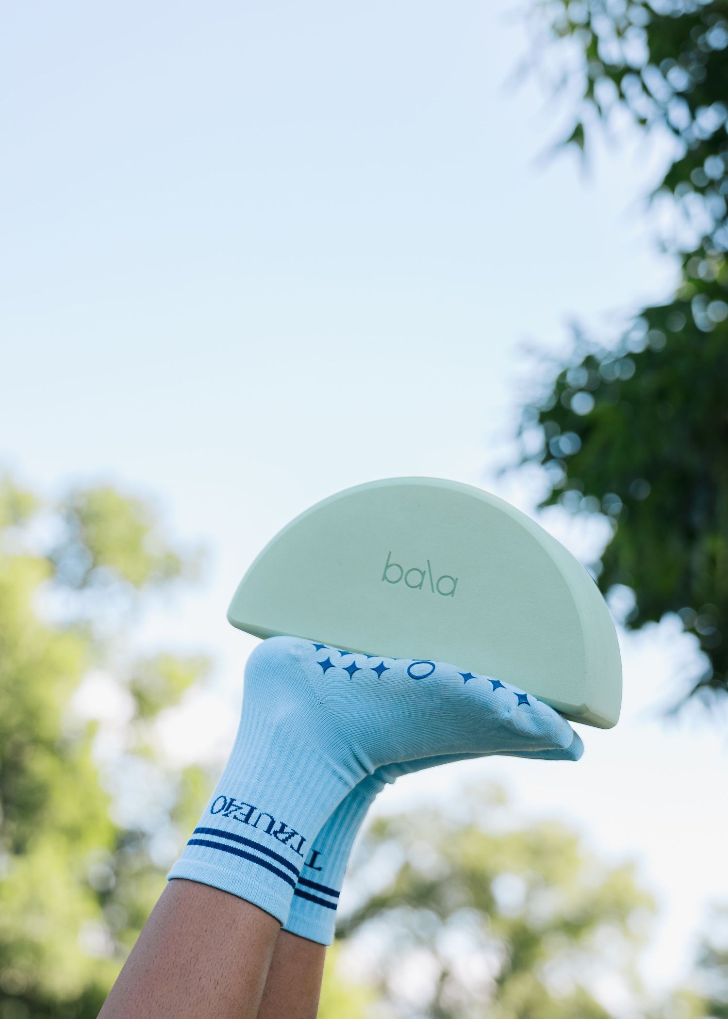 Hand wearing blue star-print socks holding a mint green Bala half-moon weight outdoors.