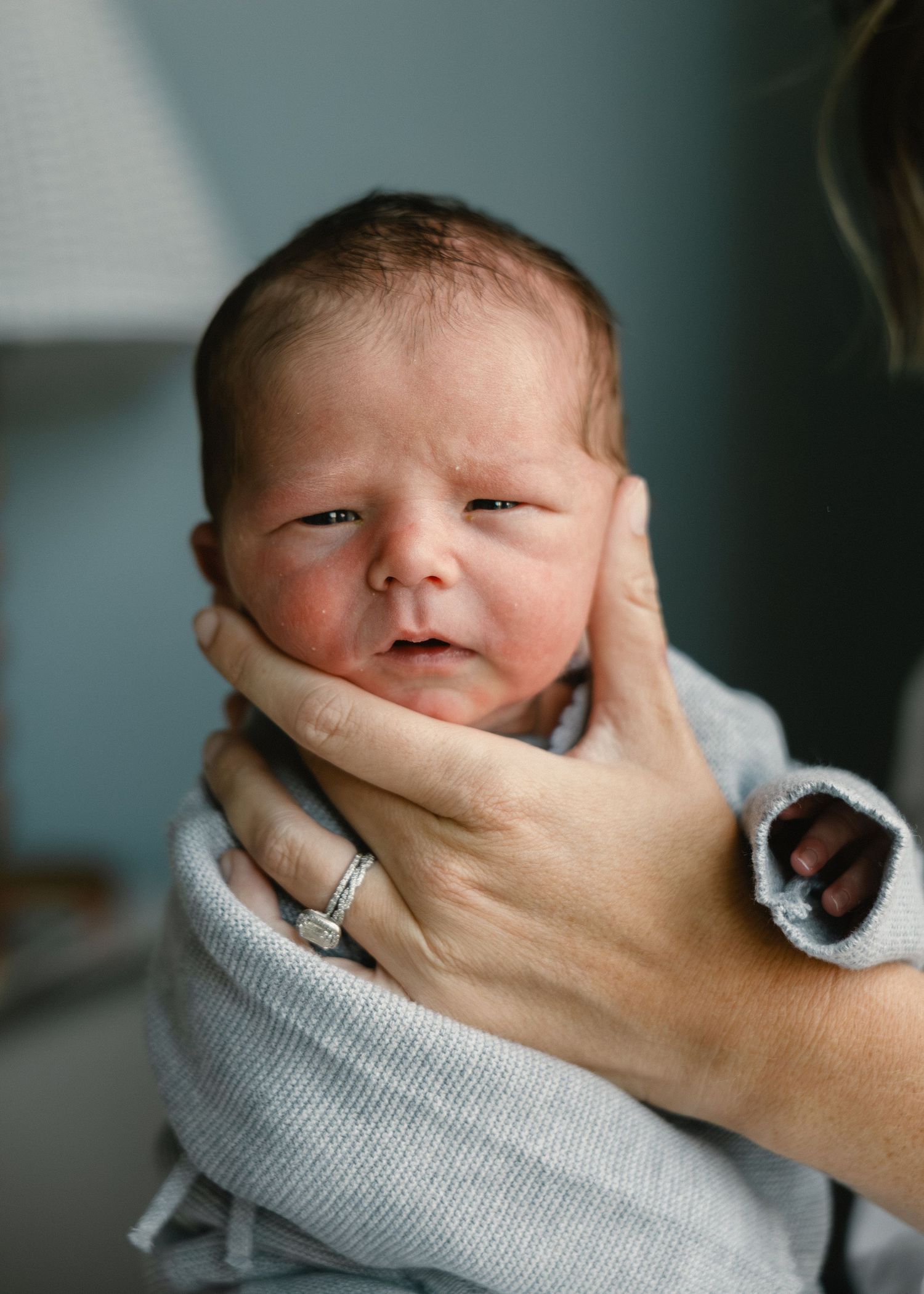 Newborn baby wrapped in light blue swaddle being gently supported by mother's hands.