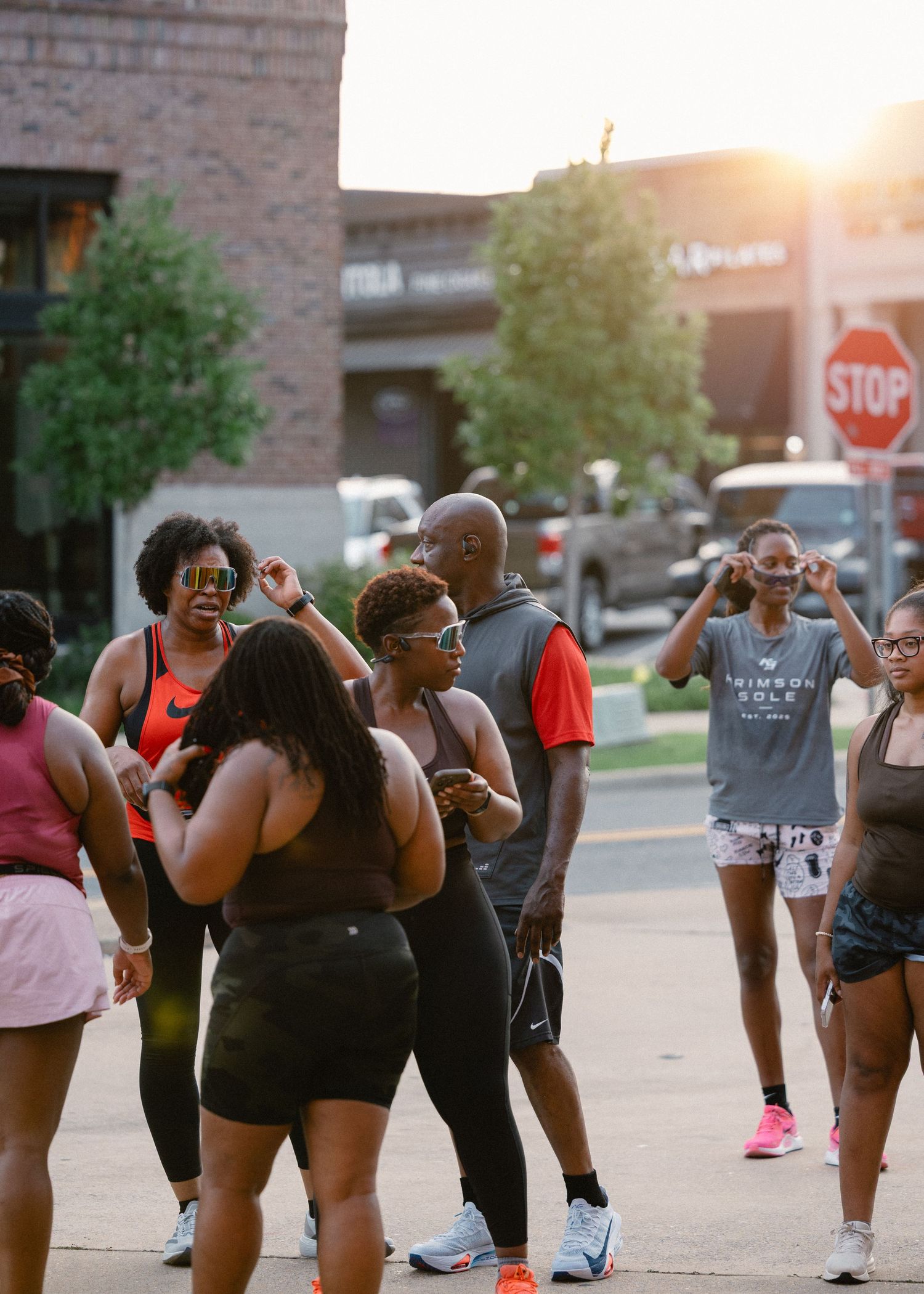 Diverse group of runners gathering on a street corner at sunset during a Krimson Sole run club.