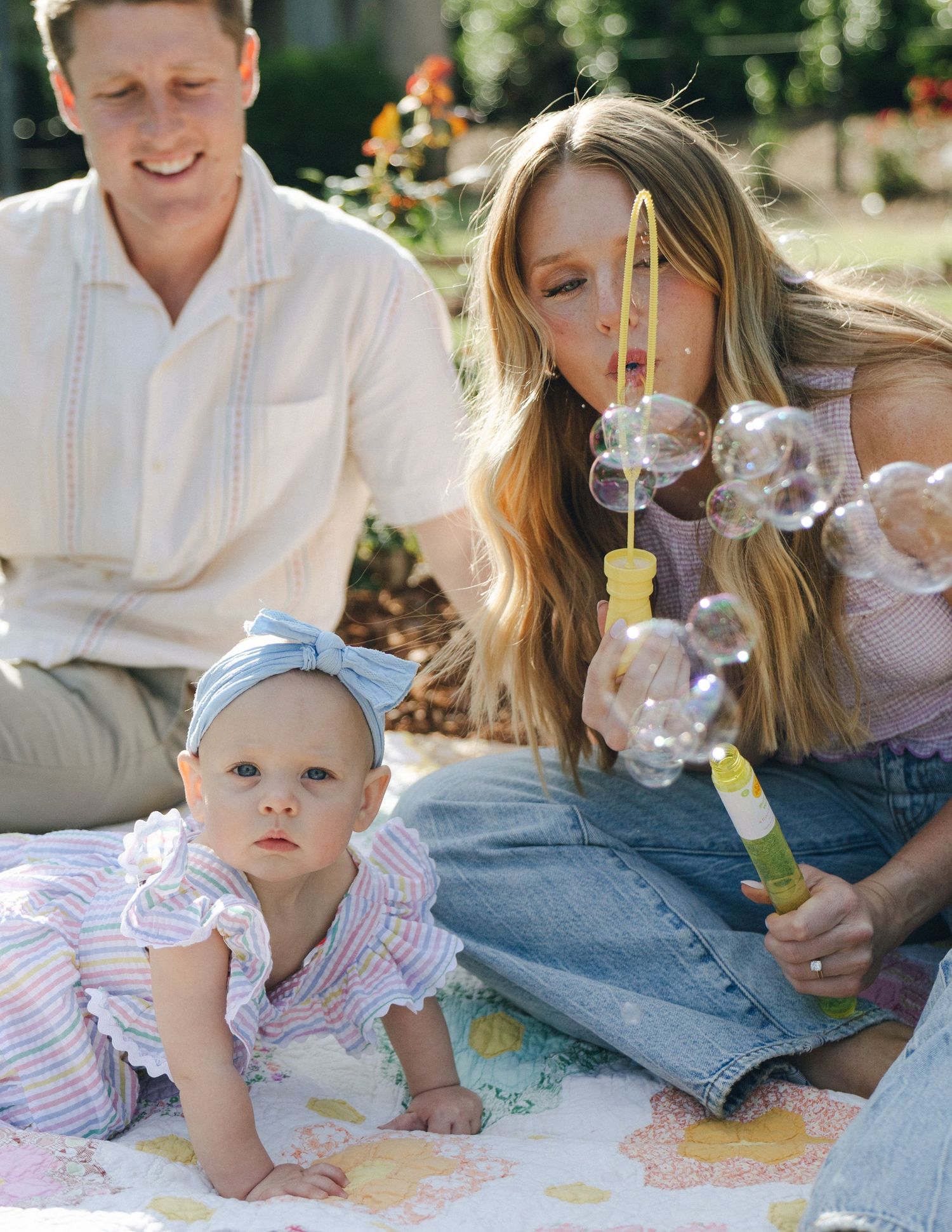 A young family enjoys outdoor playtime as mother blows bubbles for her baby girl.