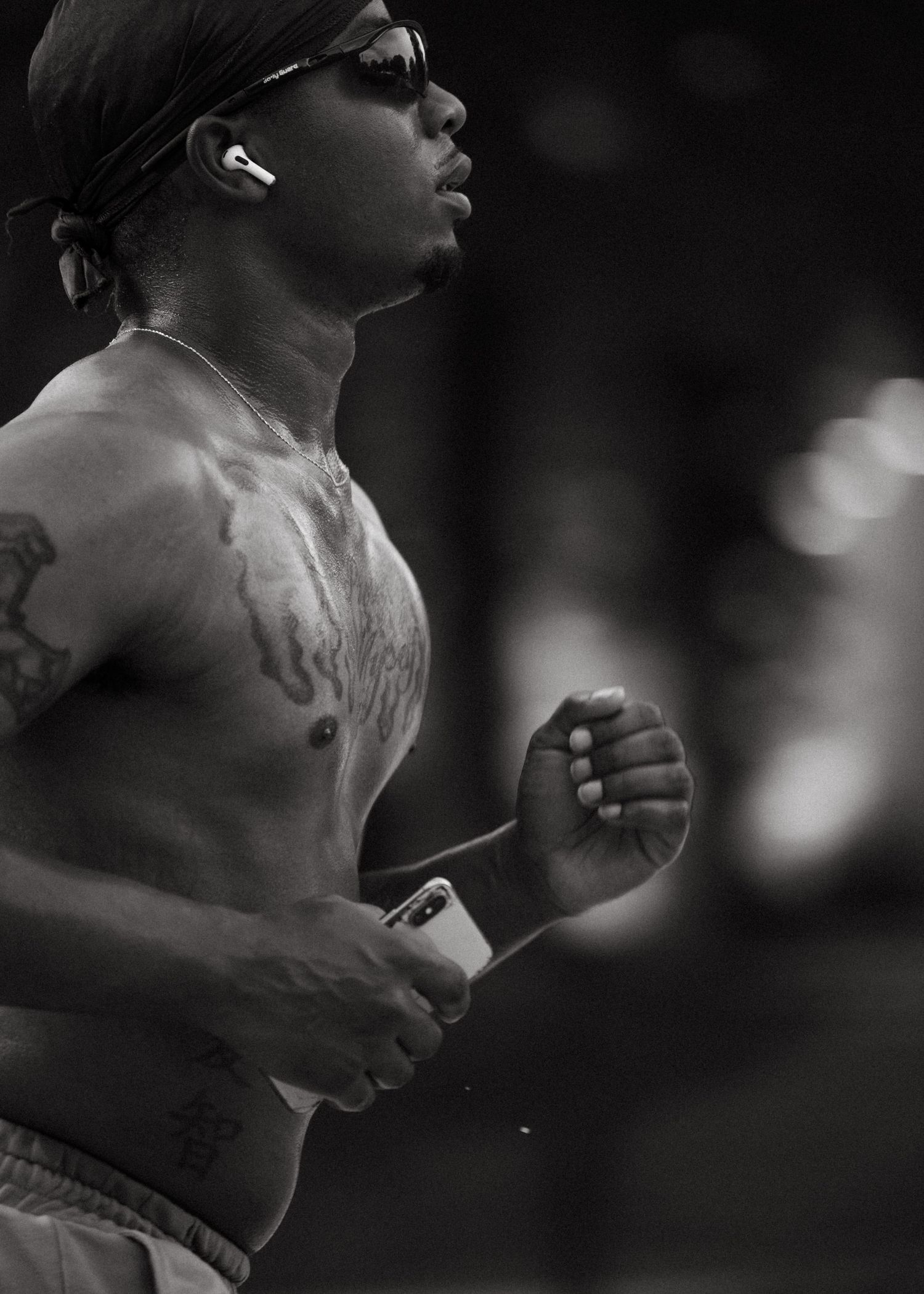 Black and white portrait of a shirtless tattooed man running with AirPods and sunglasses.