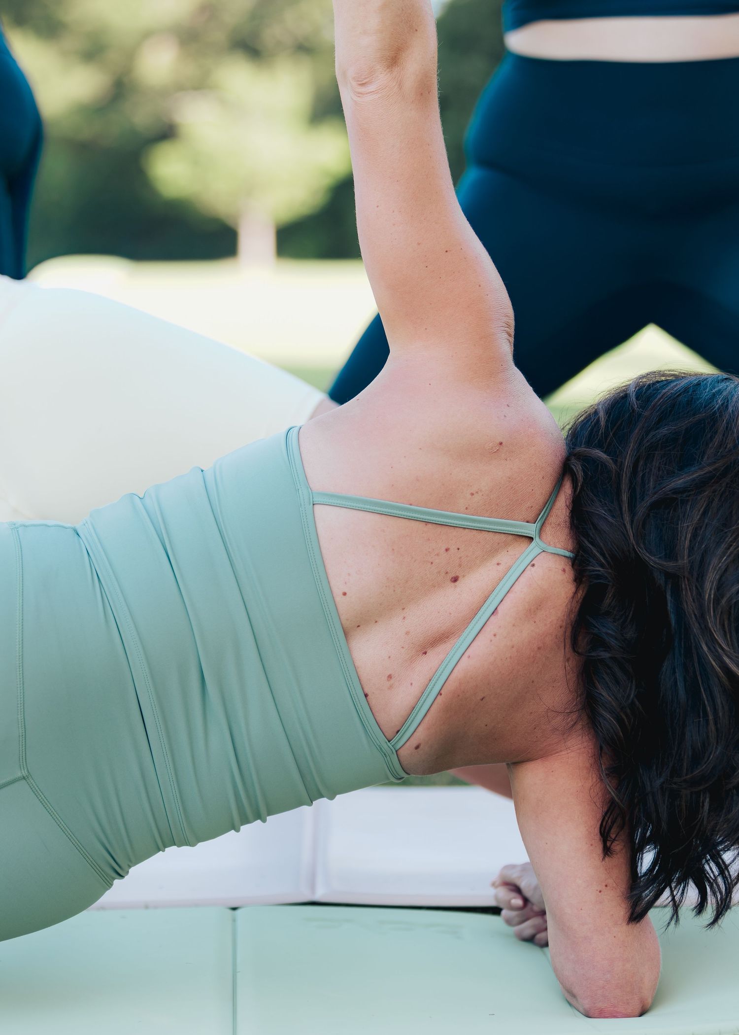 Woman in sage green sports bra and leggings performing a side plank stretch outdoors.