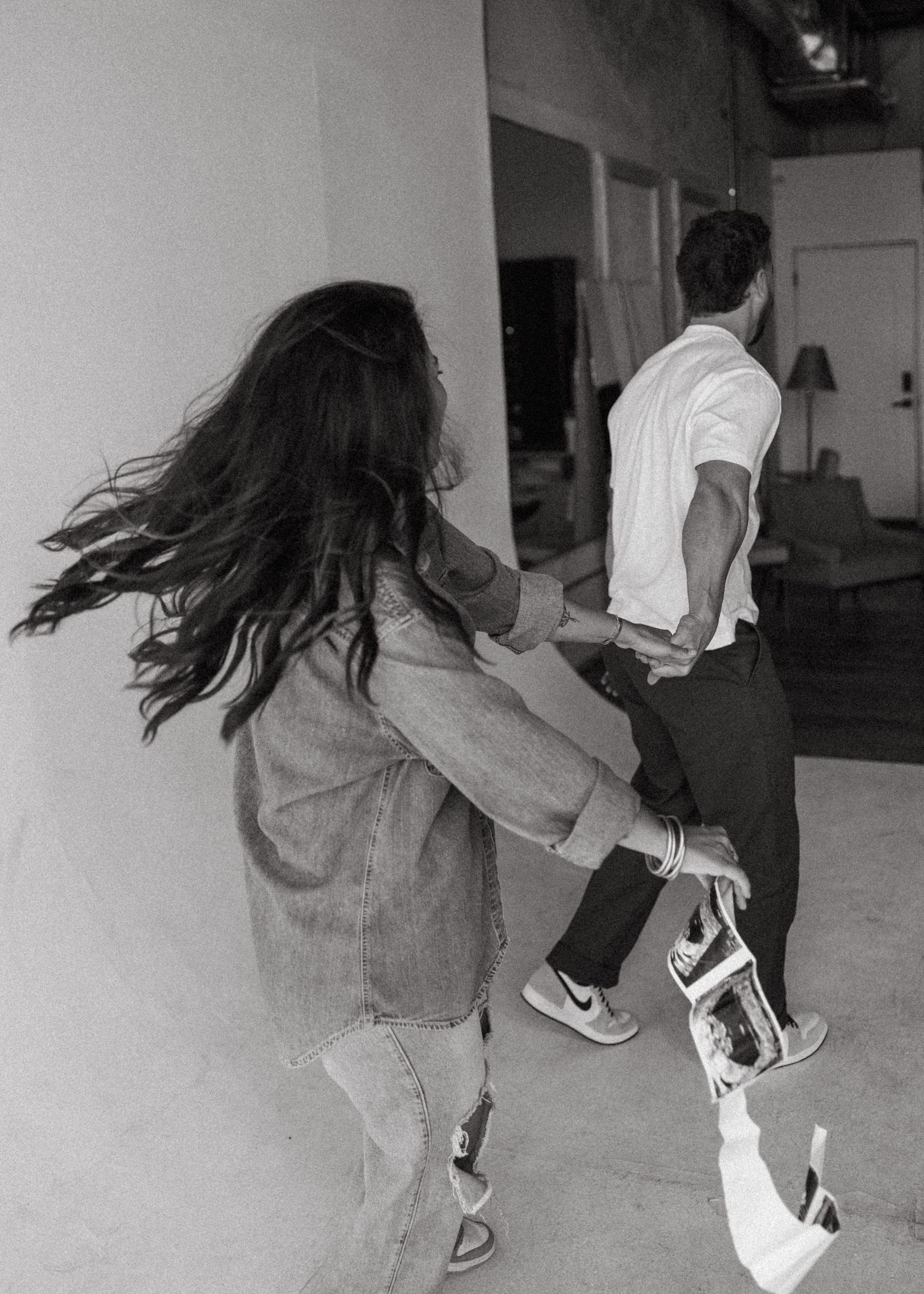Black and white photo of couple running and holding ultrasound photos in a candid pregnancy shoot.