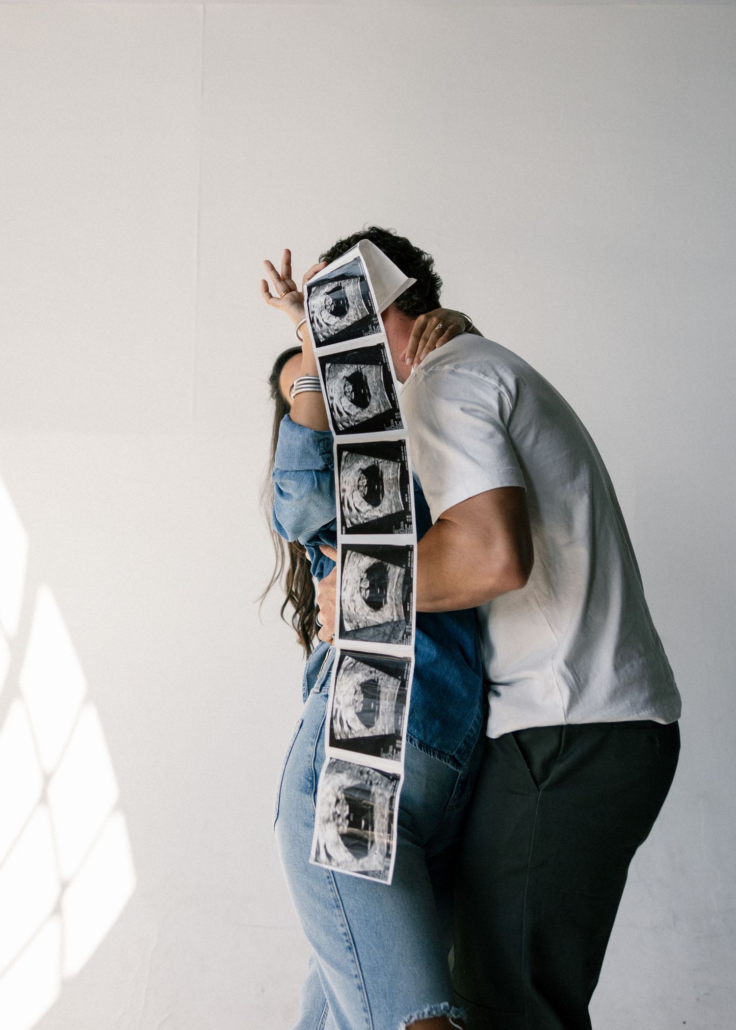 Couple sharing a kiss while holding a strip of ultrasound photos during a pregnancy announcement photoshoot.