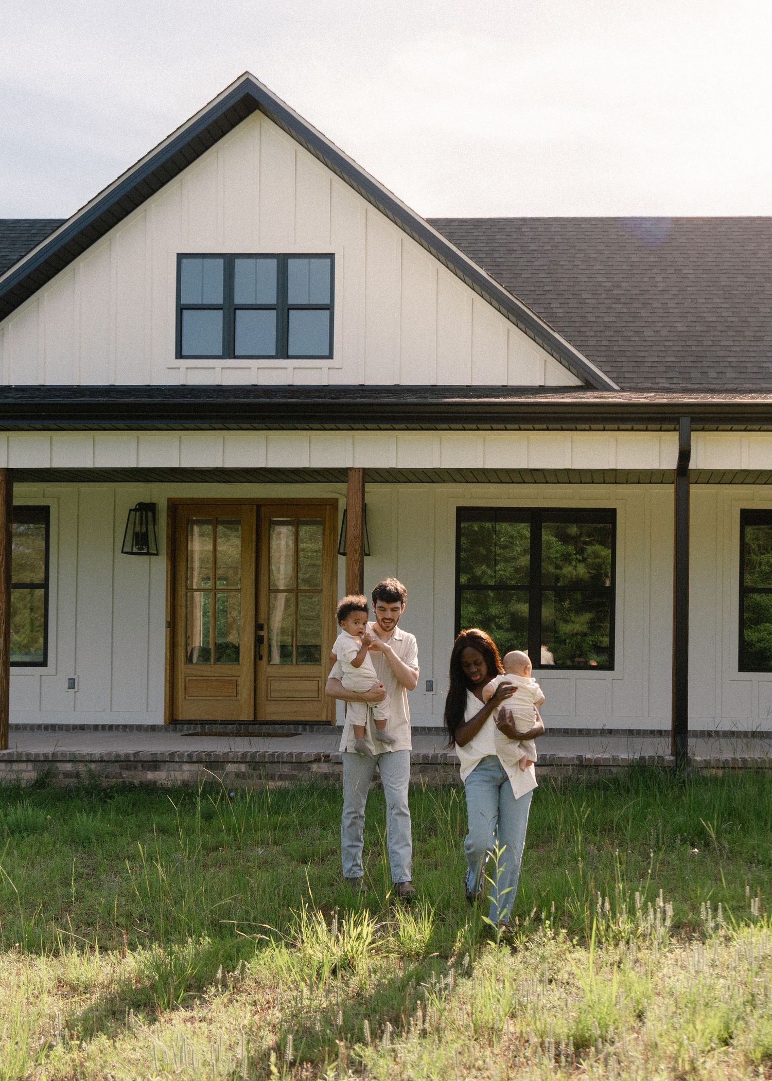 Interracial family with two young children posing in front of a modern white farmhouse.