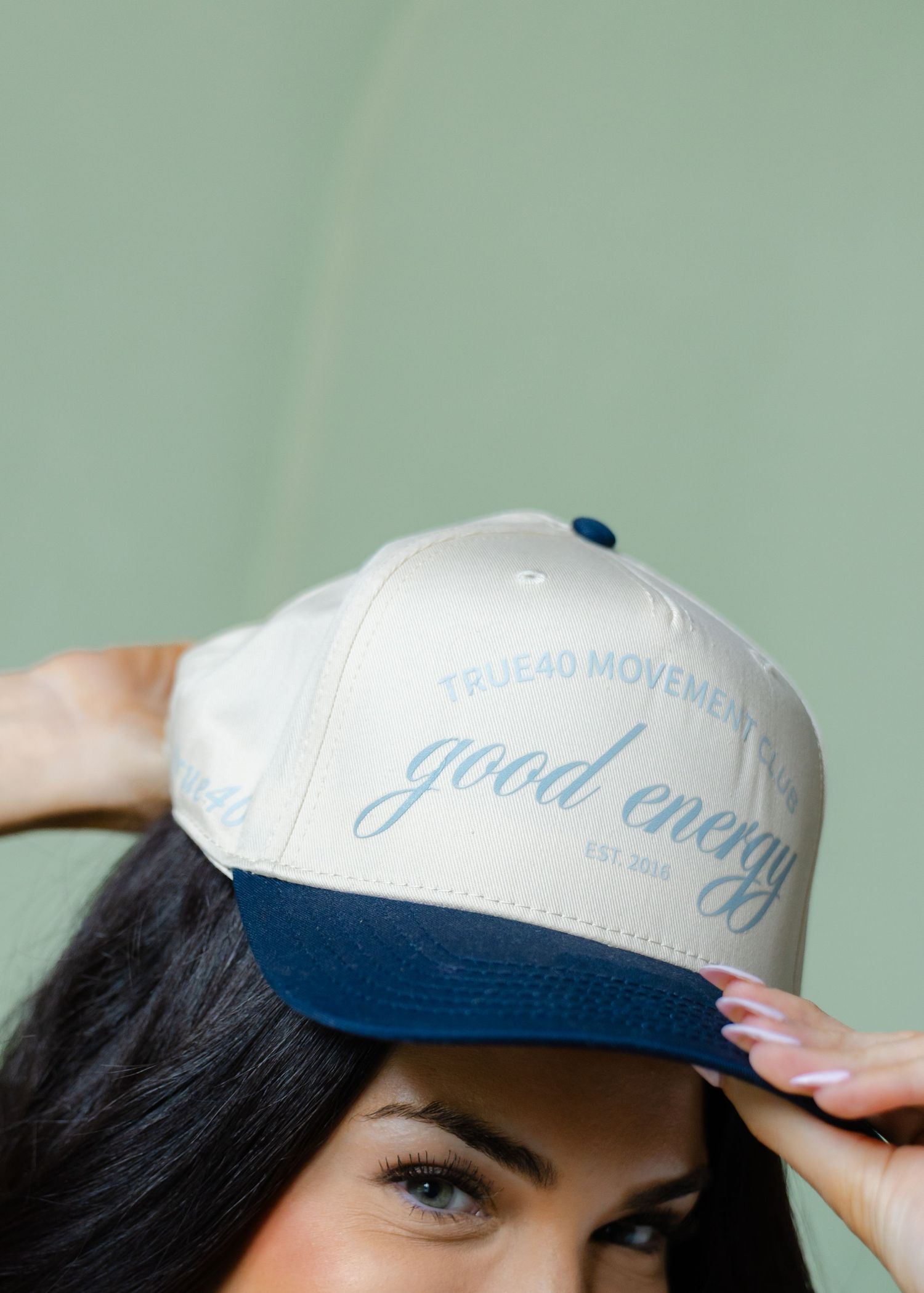 Woman wearing True40 Movement good energy snapback hat in cream and navy colors.