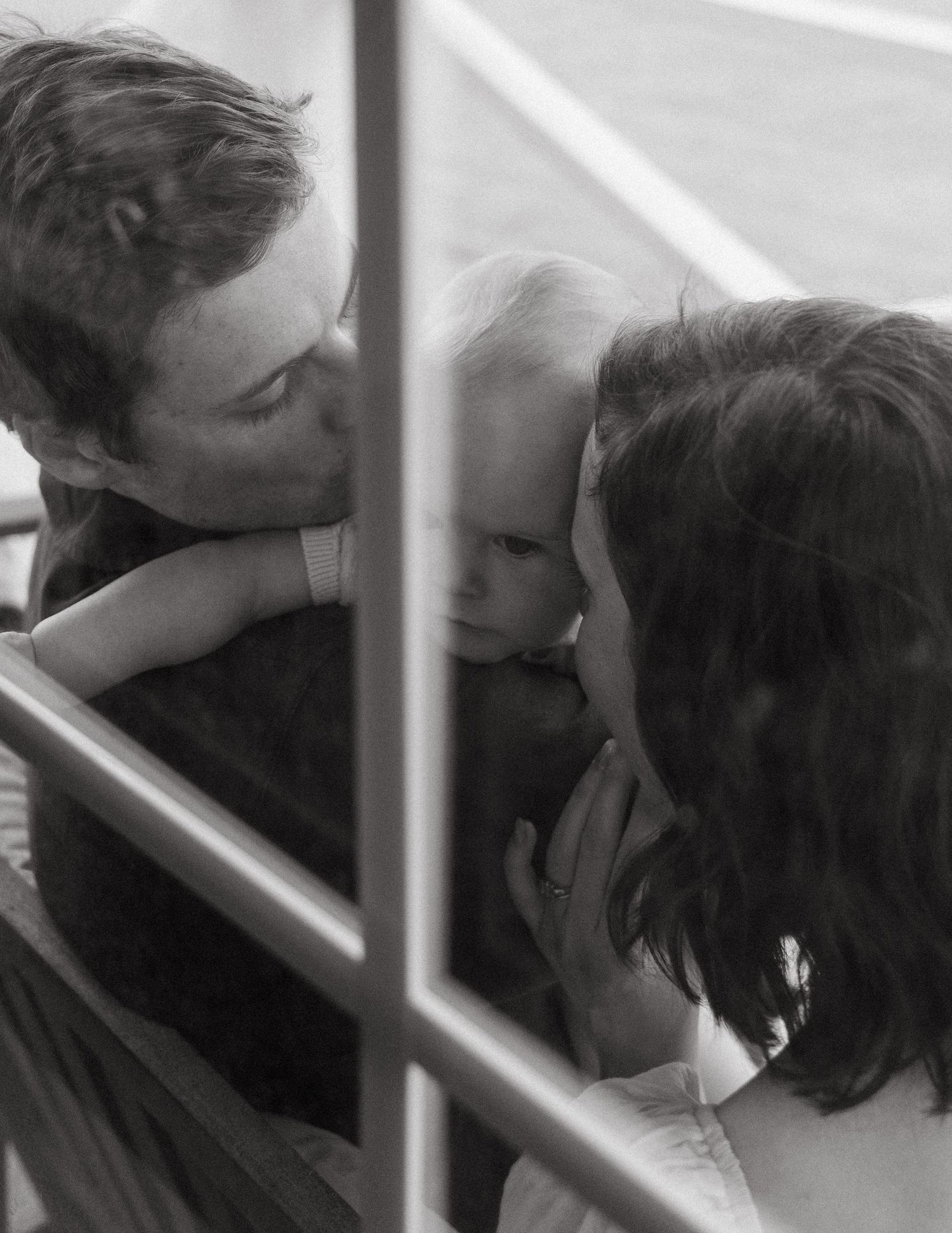 Black and white photo of parents sharing a tender moment with their baby on a porch.