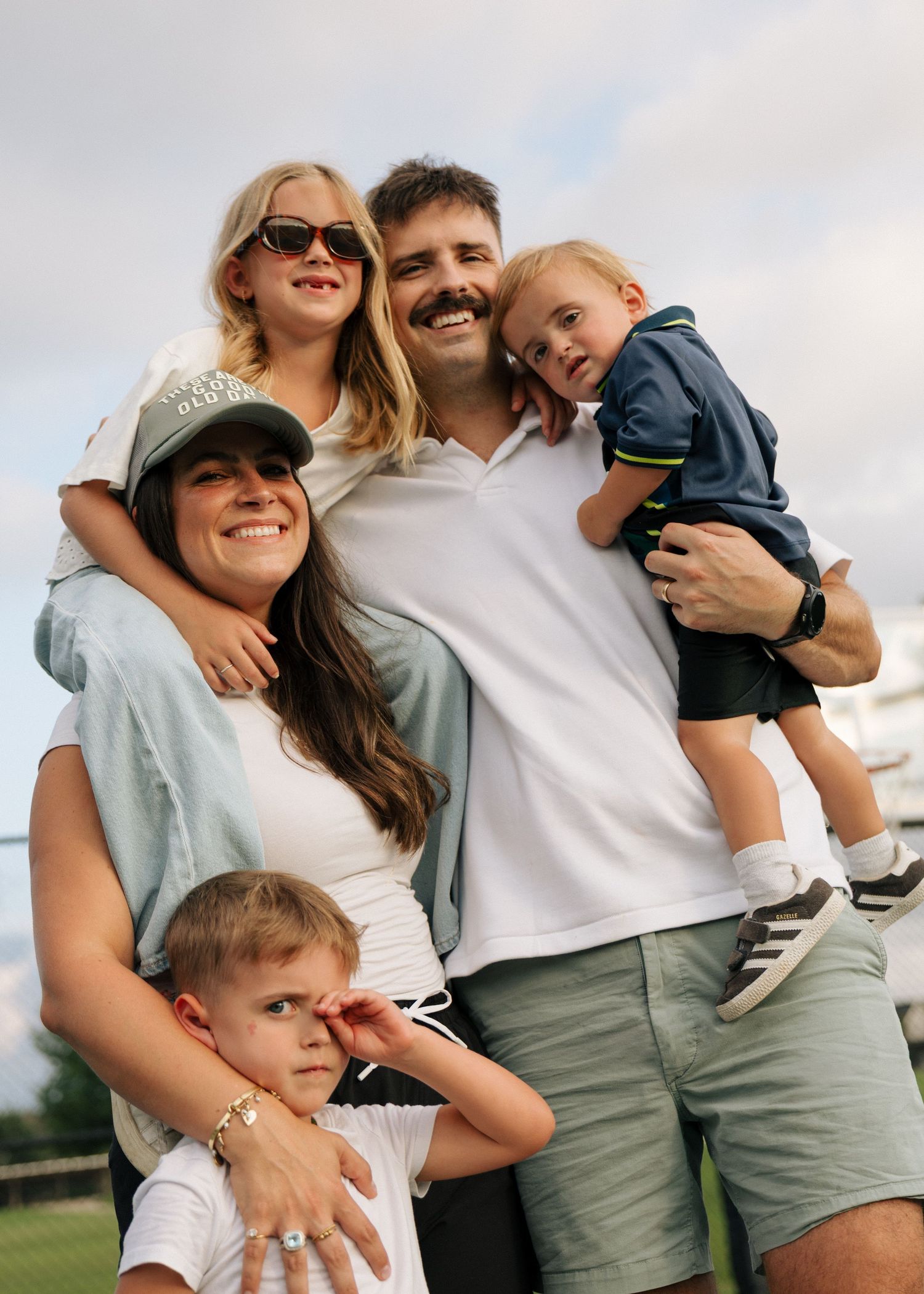 A happy family of five poses outdoors, with parents holding three young children while smiling together.