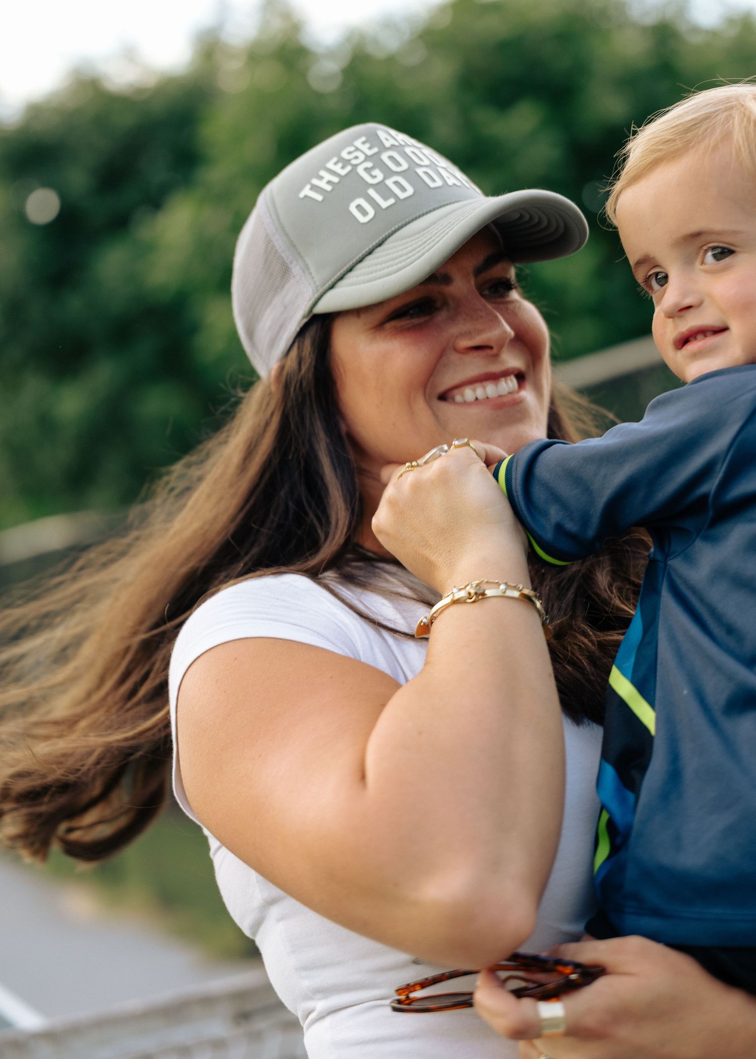 Smiling mother in baseball cap holding her young toddler son outdoors.