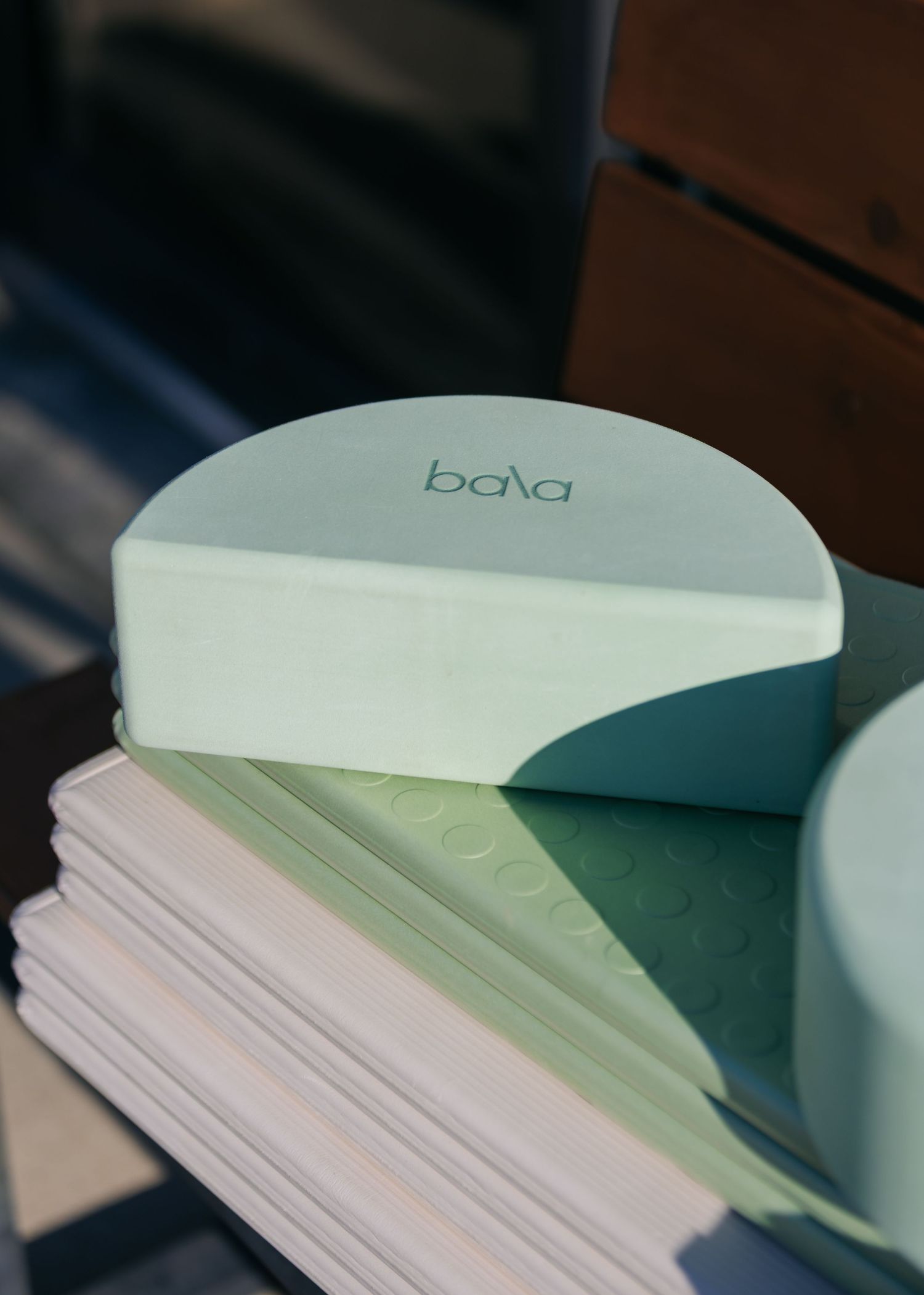 Bala brand yoga block in mint green resting on stacked exercise mats in natural sunlight.
