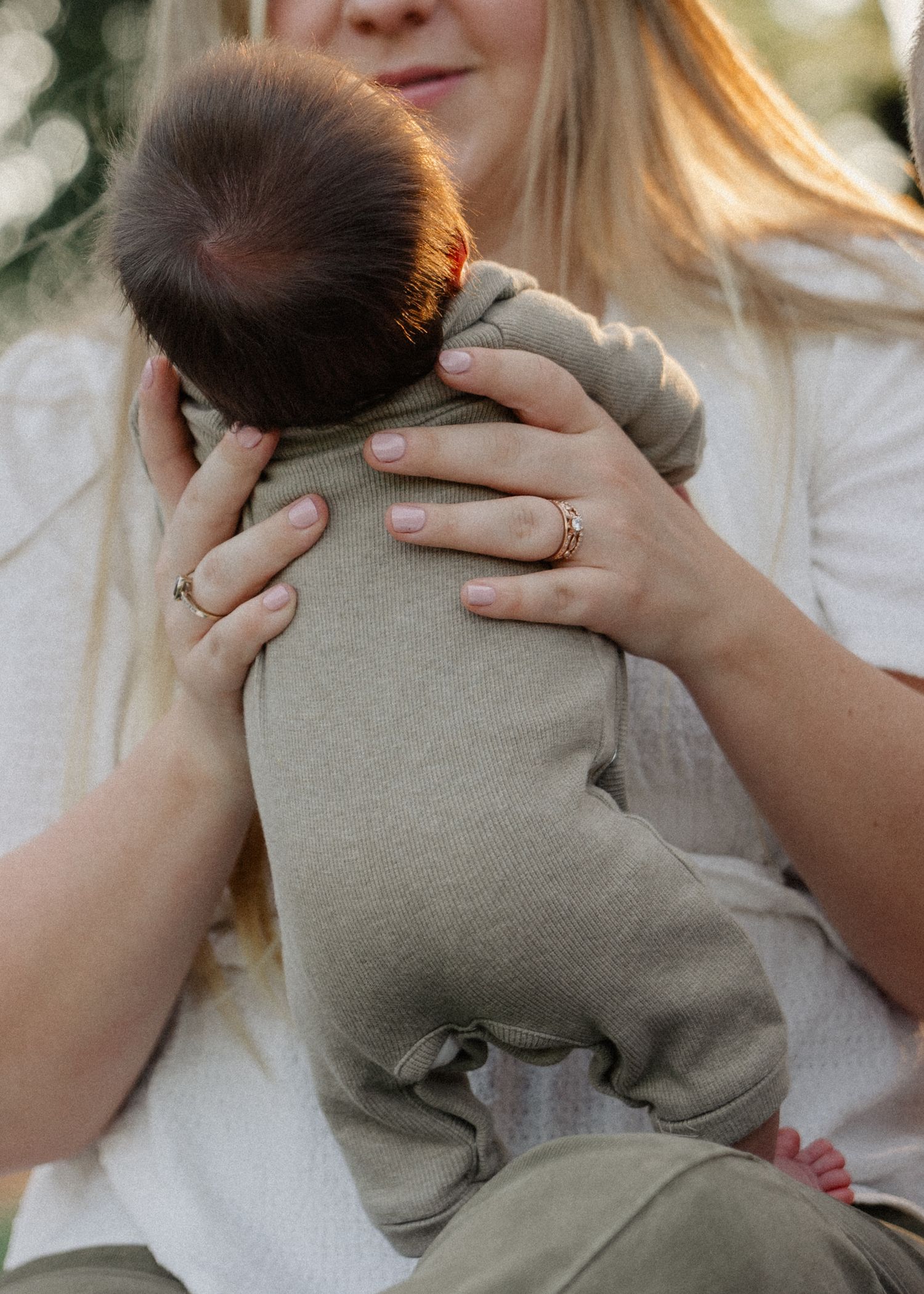 Mother in white top tenderly holding a newborn baby in an olive green outfit.